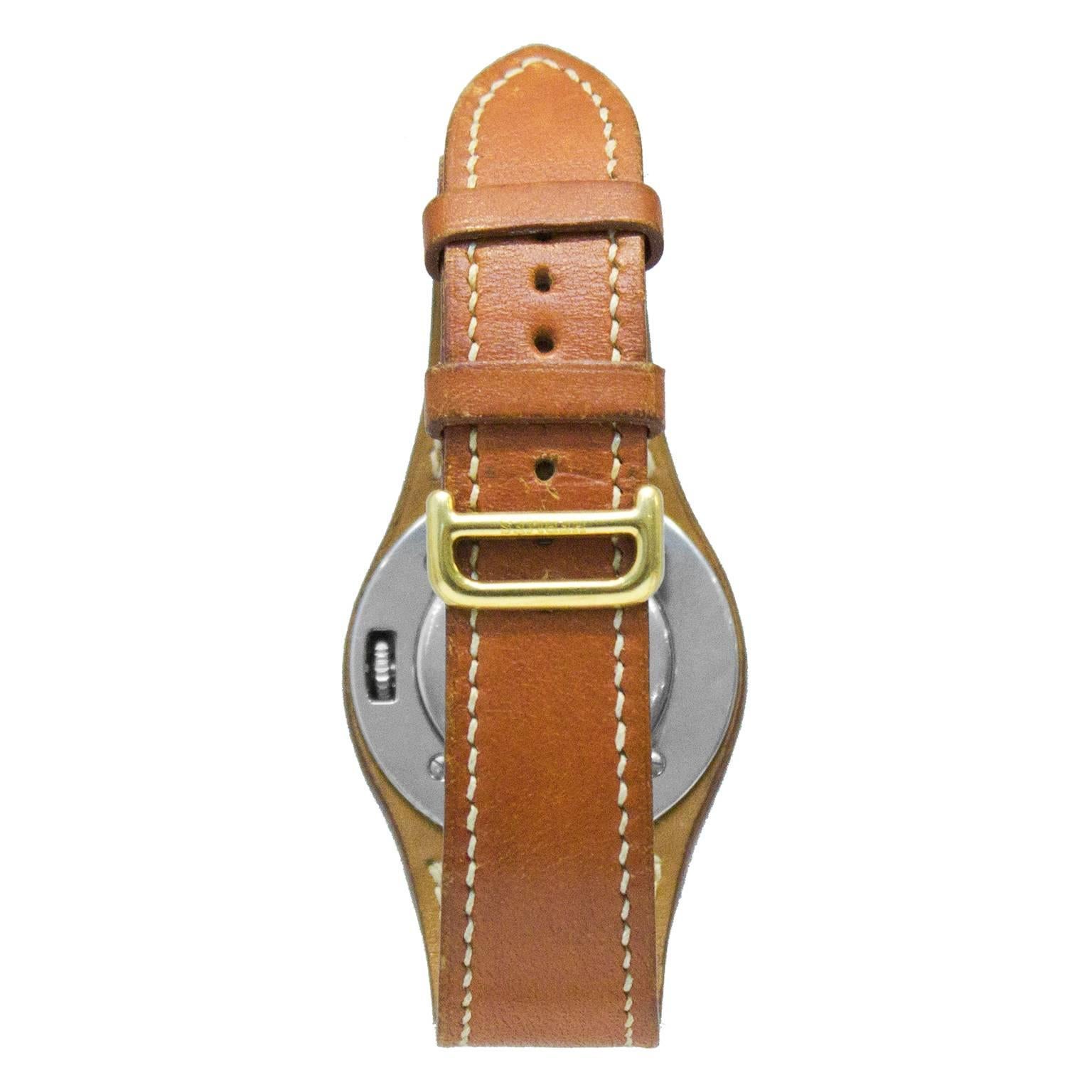 Hermes 1990's tan leather Harnais watch with beige stitching and gold hardware. The Swiss made watch features a white face with cream index hour markers and gold arms. There's a small date window at the 6’oclock position, and a concealed push/pull