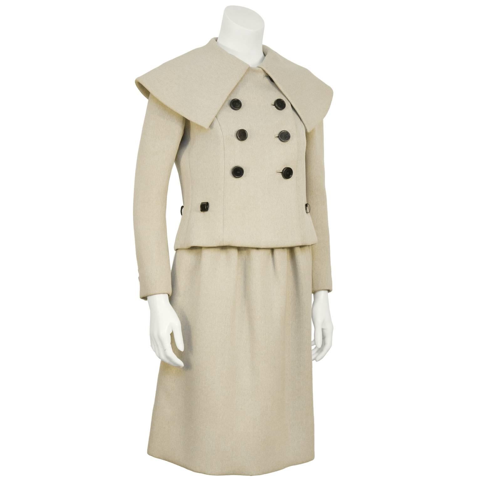 Norell beige mid-weight wool skirt suit from the 1960's. The double breasted jacket features a pilgrim collar and 6 large black circular buttons down the front. The black patent leather belt loops on the front and the side fits a skinny belt.