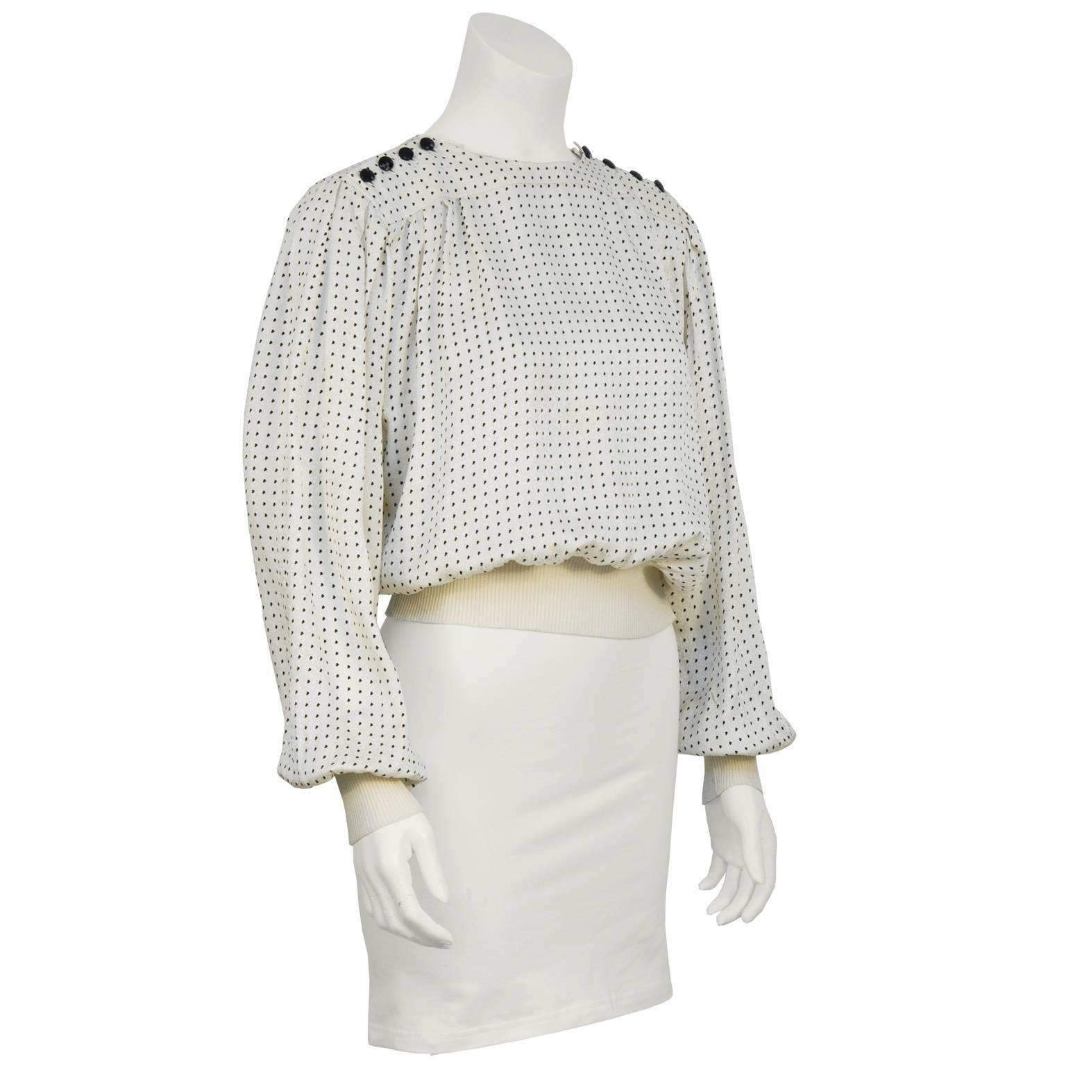 Emanuel Ungaro off white and black silk polka dot blouse from the 1980's. The blouse features a yoke neckline with four black faceted round buttons on either shoulder. The hem and cuffs are finished in cream ribbed knit. The top has pleating along