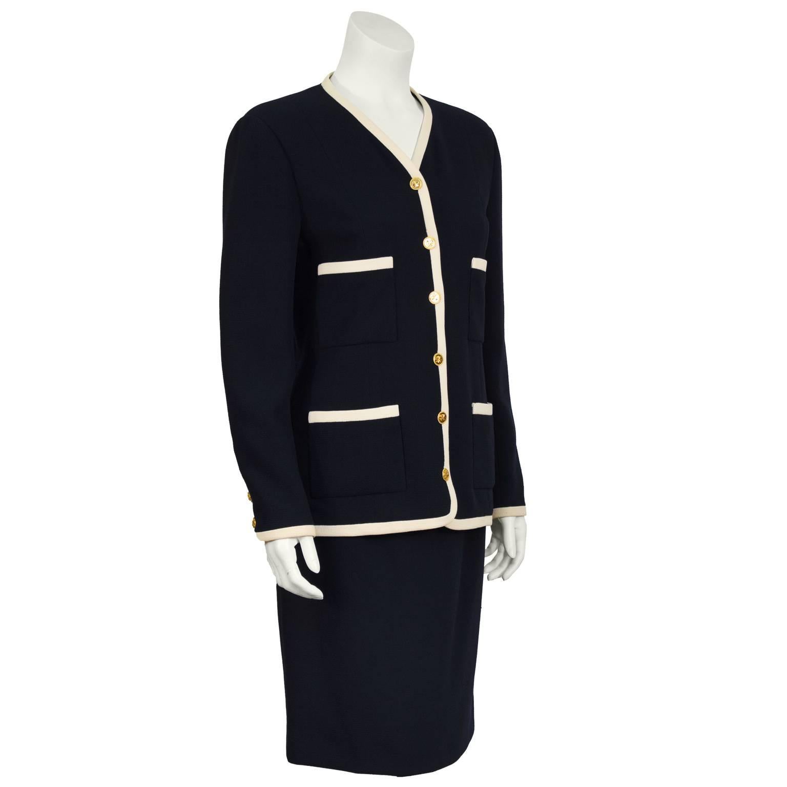 Chanel wool crepe navy suit from the 1980's. The slightly fitted jacket features four front pockets trimmed in white with gold cloverleaf buttons on the front and cuffs, fully lined in silk. Off white trimming throughout. The skirt does up the back
