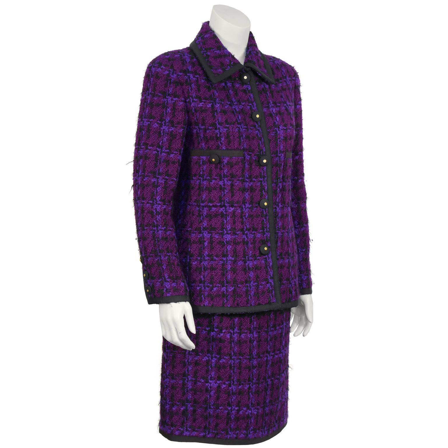 Chanel purple and black plaid boucle skirt suit from the 1980's. The jacket has a pointed collar and two patch pockets on the front that are trimmed in black grosgrain ribbon. Front closure up with grosgrain covered buttons adorned with gold CCs at