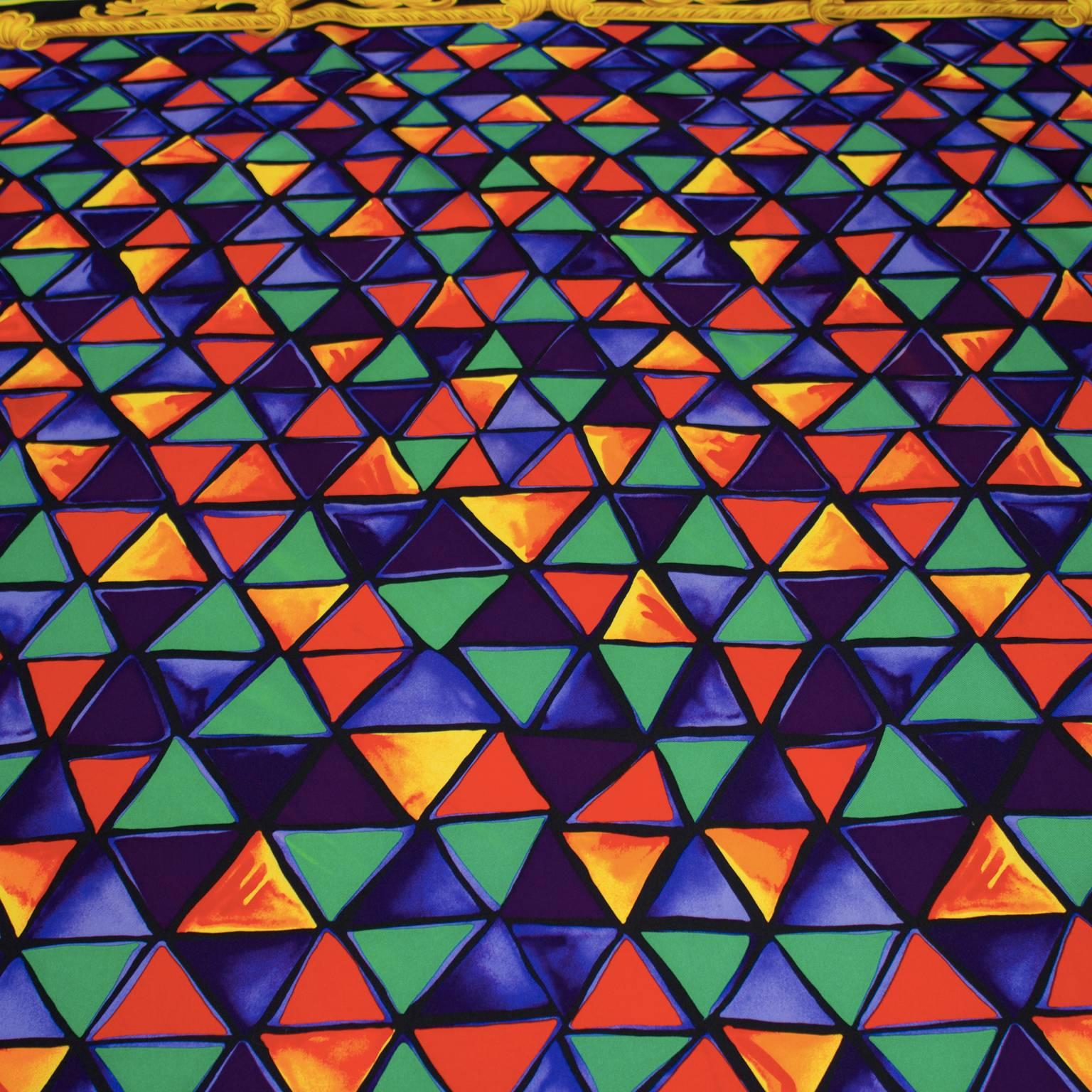 Triangular patterned jewel tone silk scarf by Versace circa1980's. The green, blue, orange and red triangles scale from small to large from top to bottom and are bordered in a gold frame. The scarf is finished with two borders; a dotted one