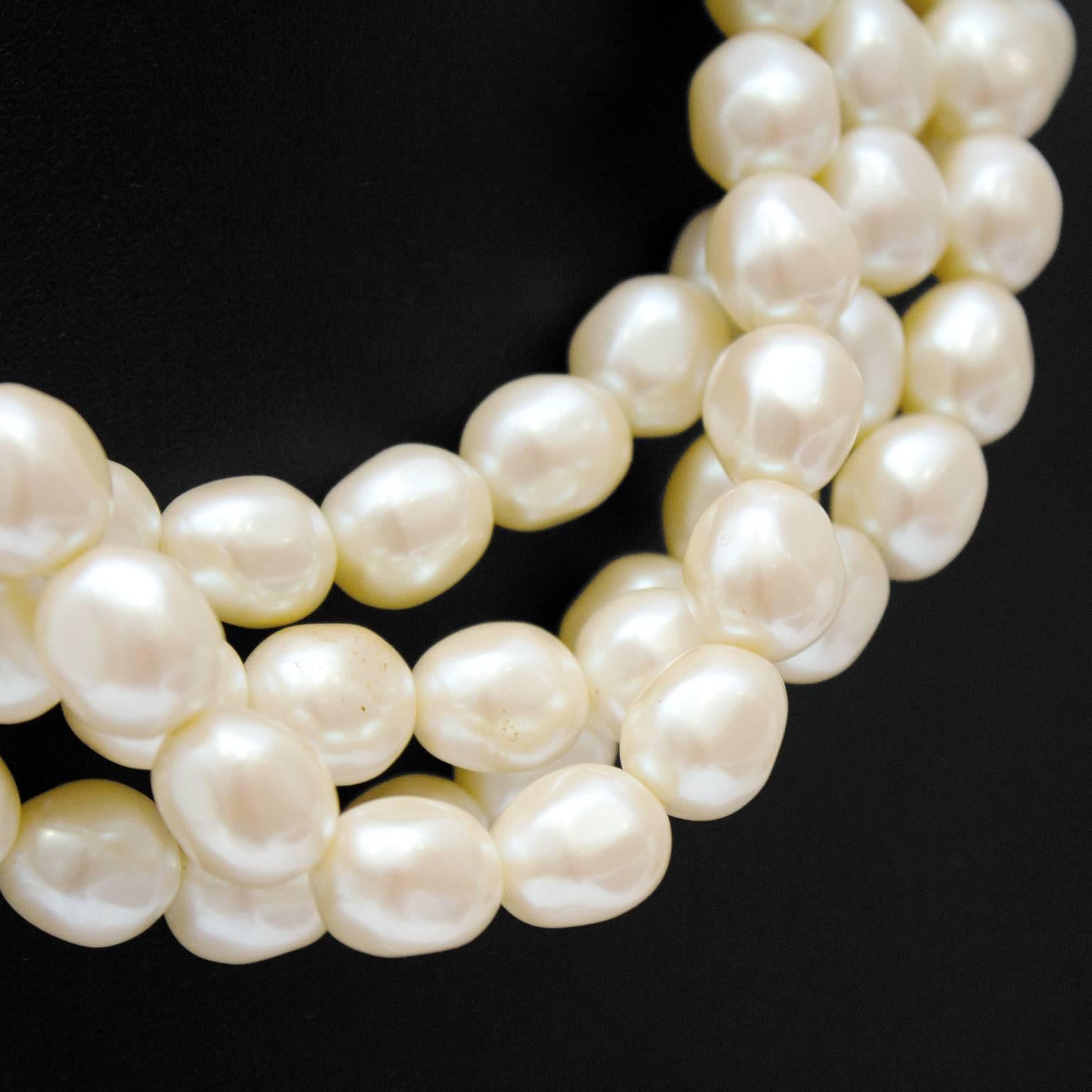 1980's YSL four-strand faux pearl necklace. This statement piece fastens with an art-deco inspired clasp that lies flat and is adorned with a large pearl cabochon. Excellent condition. Meant to worn twisted or casually draped, clasp front or