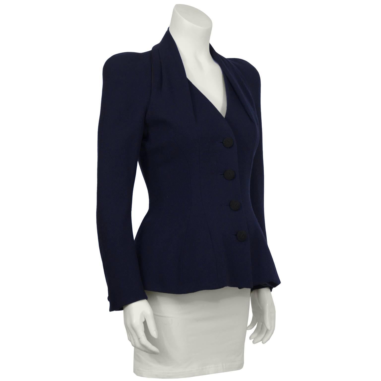 John Galliano 1990’s deep navy wool crepe bar jacket. The jacket features sculpted shoulder pads and a pleated draped neckline that blends into the bust. It is fitted through the waist and has padded hips. Fastens up the front with unique black