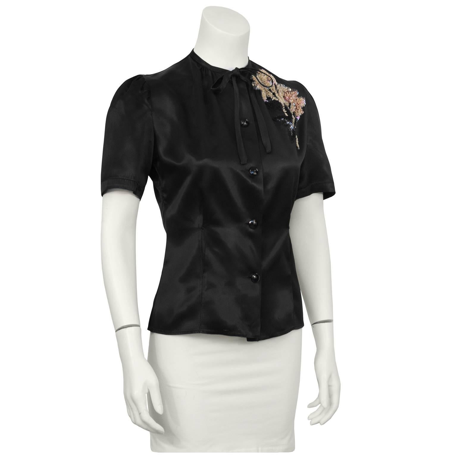 The best 1940's satin black fitted blouse with hand sewn sequin bouquet appliqué. The blouse features a skinny self tie bow and jet black faceted buttons down the front with a feminine puff sleeve. Fitted through the waist. In excellent condition.