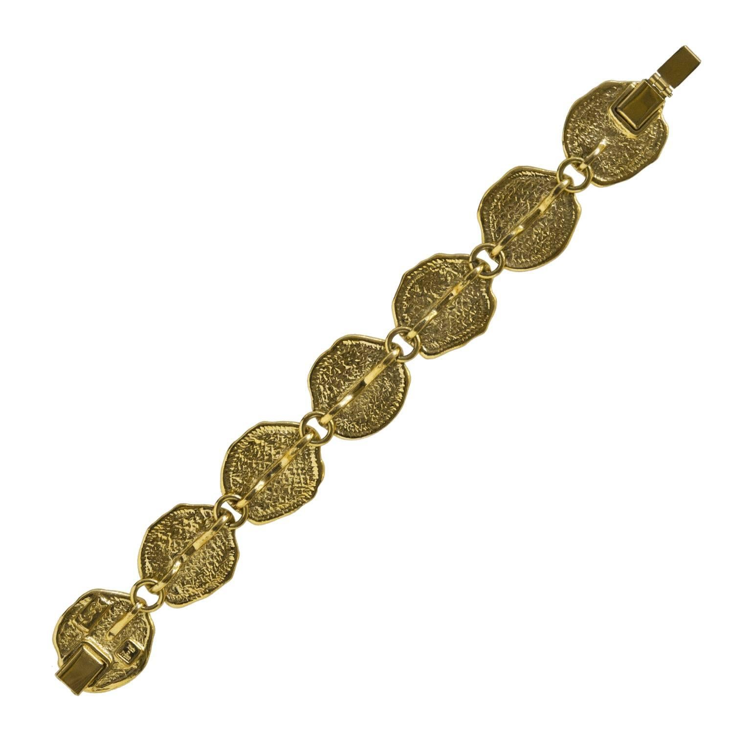 Yves Saint Laurent 1980's gold plated medallion link bracelet. The medallions feature abstract fossilized impressions of scrolls and the profile of a head. Signed YSL and made in France. Tab inset clasp. In excellent condition. 