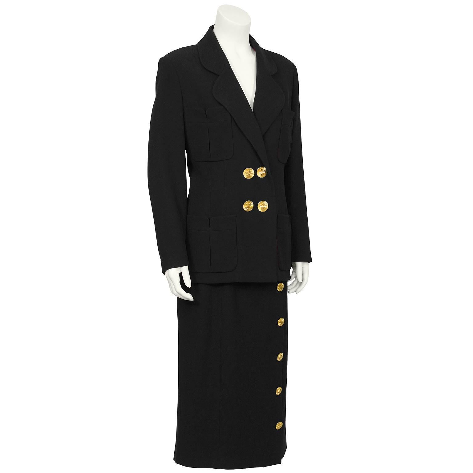 The ultimate 1980's Chanel black maxi suit. The jacket has a curved notched lapel with similar curved details on the pockets and fastens double-breasted at the front with oversized gold-toned cloverleaf buttons. Matching buttons on the cuffs. The