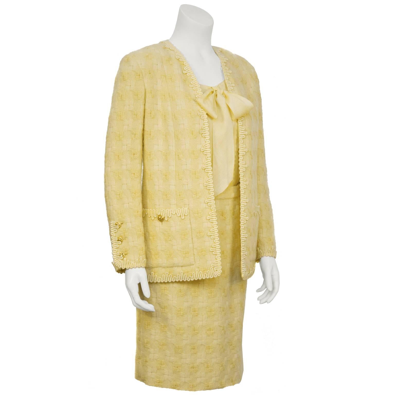Chanel 1970's butter yellow woven wool skirt suit. The jacket features rickrack trim along the pockets, cuffs and edges and is finished with gold basket weave detail buttons. The skirt fastens up the back with a zipper and snap. The matching yellow