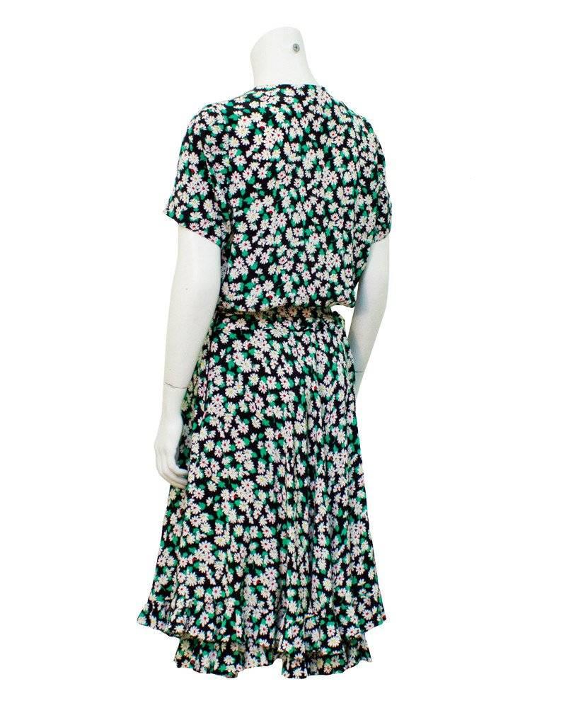 Classic Albert Nipon silk floral daydress from the late 1980s. The black dress has an all over pattern of green and white flowers with a touch of red. There is a sweet black bow at the neck and black buttons go down the front of the dress. A