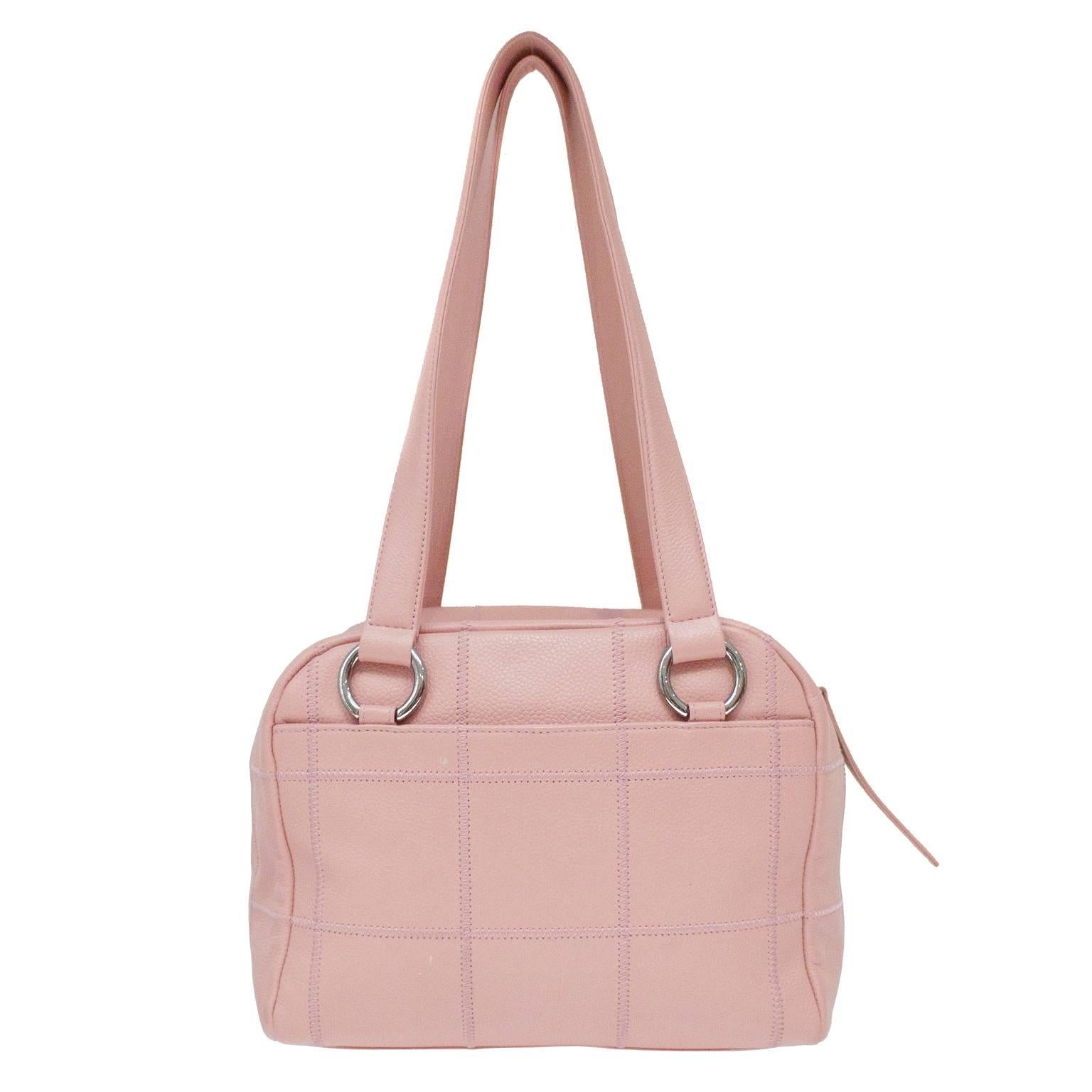 Pink pebbled leather bowler style bag with a stitched grid detail from the mid 2000's. The bag has two top handles that are attached with rings to a silvertone CHANEL plaque. The bag opens with a top zip that has a pink leather pull tab and the