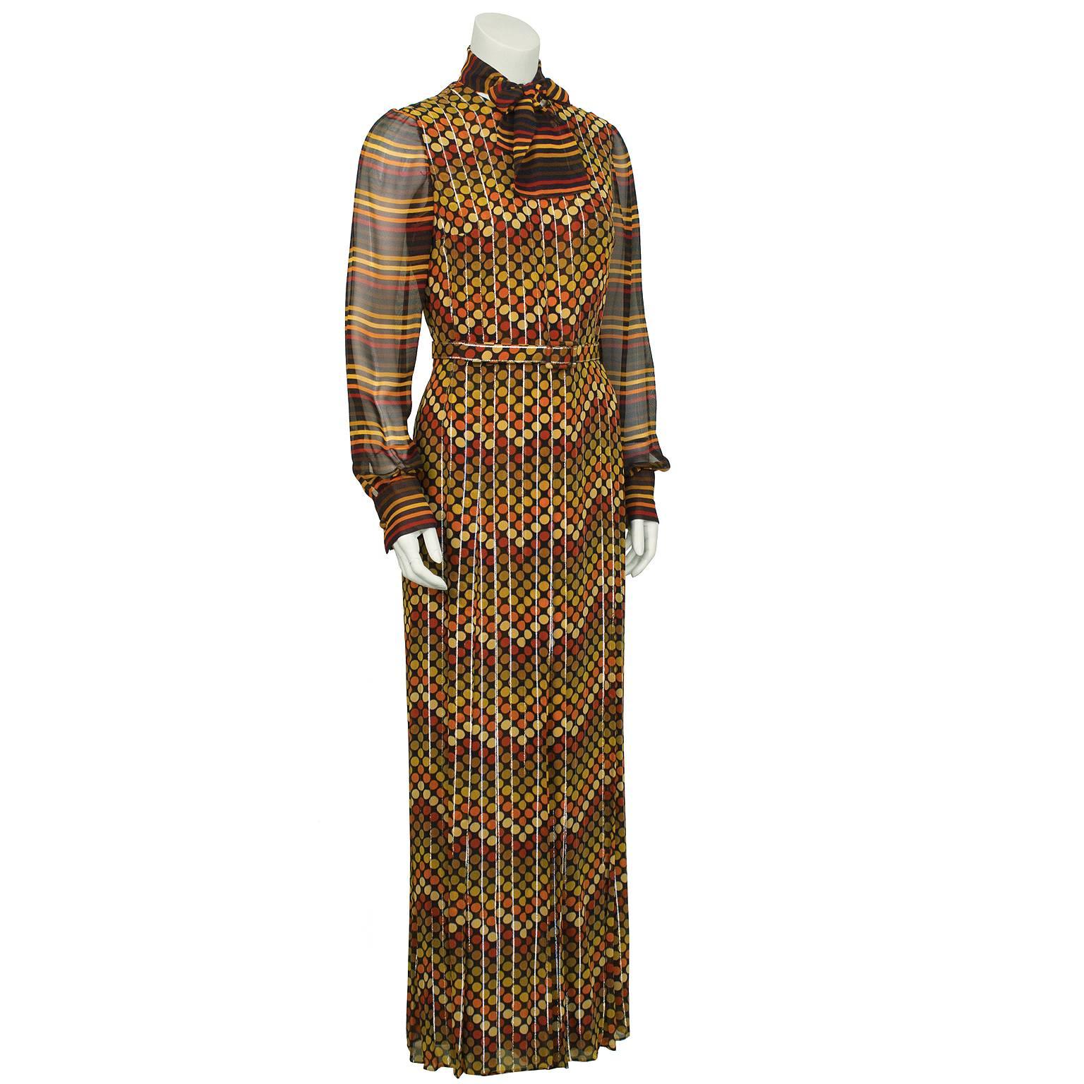 Orange, yellow and silver Italian jacquard silk gown on brown background from the 1970’s with a matching striped neck scarf. The gown has a high rounded neckline and is fitted through the body. The pleated skirt falls from the waist, partially