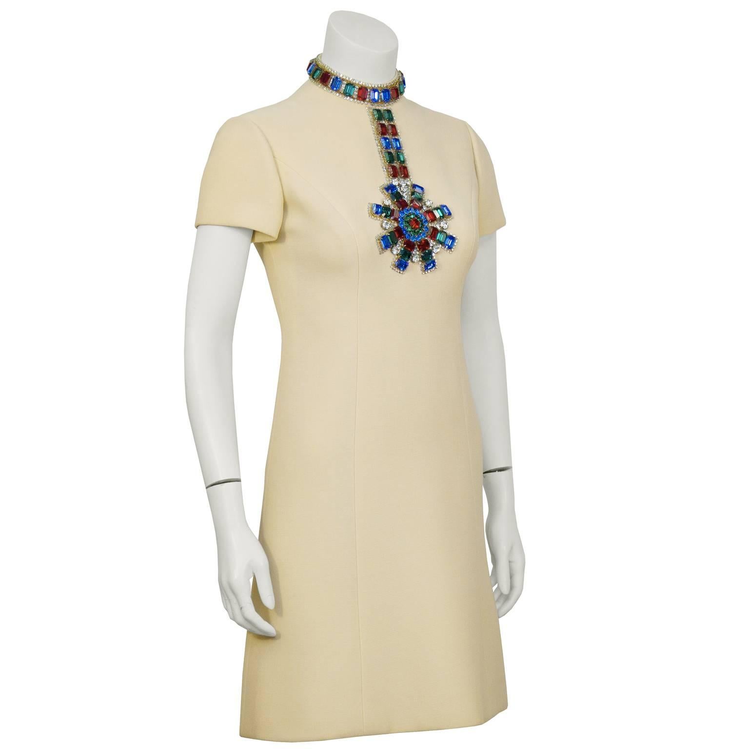 A stand out piece from the 1960’s, this Norell off white cocktail dress with large jewel embellishment needs no accessories.  The classic A line shaped dress, made from mid weight wool. The high neckline and front bodice is adorned with large green,