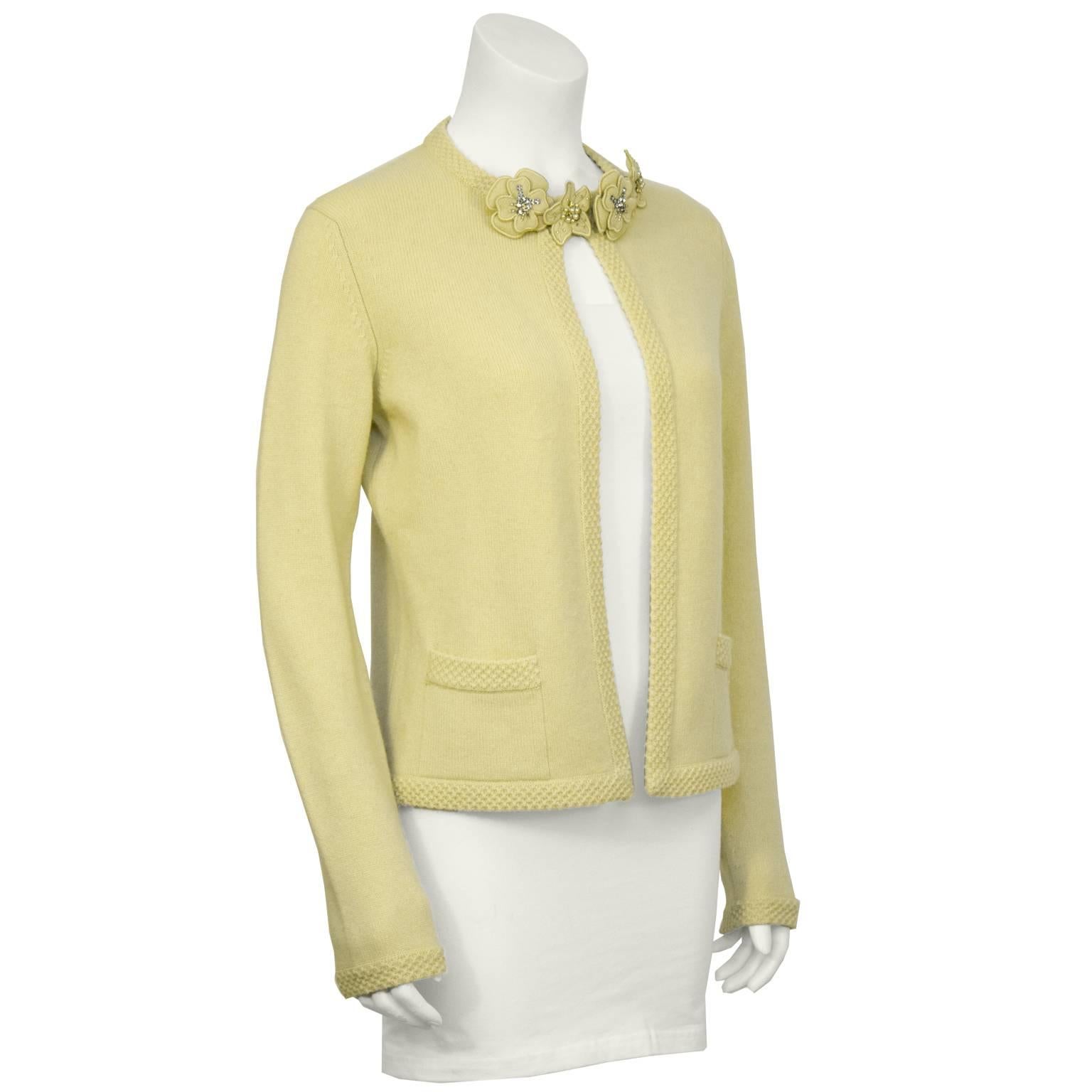 Spring 2005 Chanel butter yellow cashmere cardigan. The cardigan has a hook closure at the neck, two front patch pockets, and a cashmere honeycomb trim. The neckline is adorned with four cashmere flower pins with rhinestones and pearls that are
