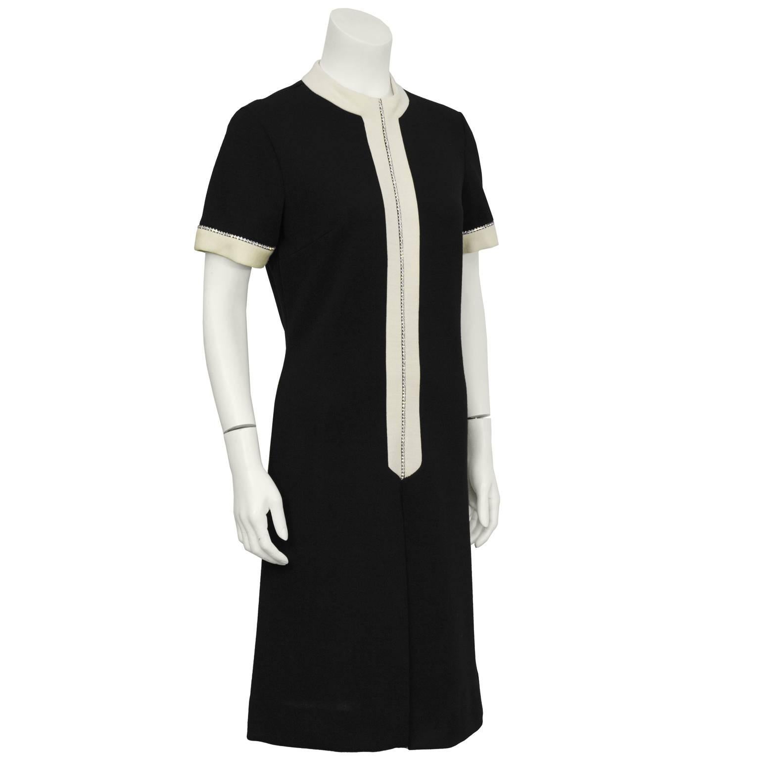 strickkleid aus den 1960er Jahren mit strassbesetztem Detail. Das Kleid hat einen hohen Kragen mit cremefarbener Strickleiste, die vorne und an den Manschetten mit einem Strass-Detail verziert ist. Umgekehrte Falte auf der Vorderseite und