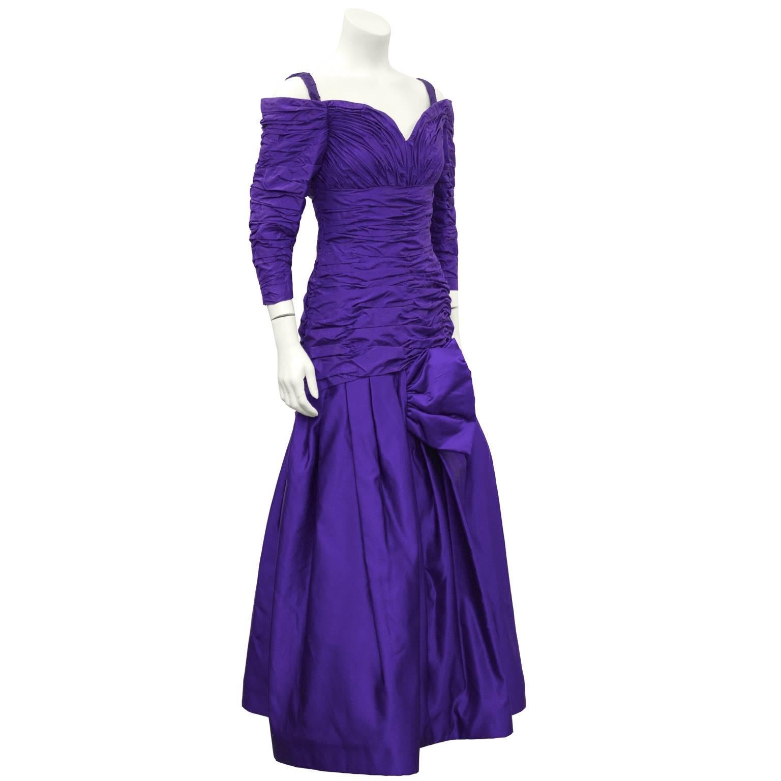 Purple ruched Arnold Scaasi evening gown from the 1980's. Sweetheart neckline, elastic shoulder straps, 3/4 length sleeves and a drop waist. Fitted through the body with a full skirt and a bow detail on the lower left hip. Zips up the back, attached