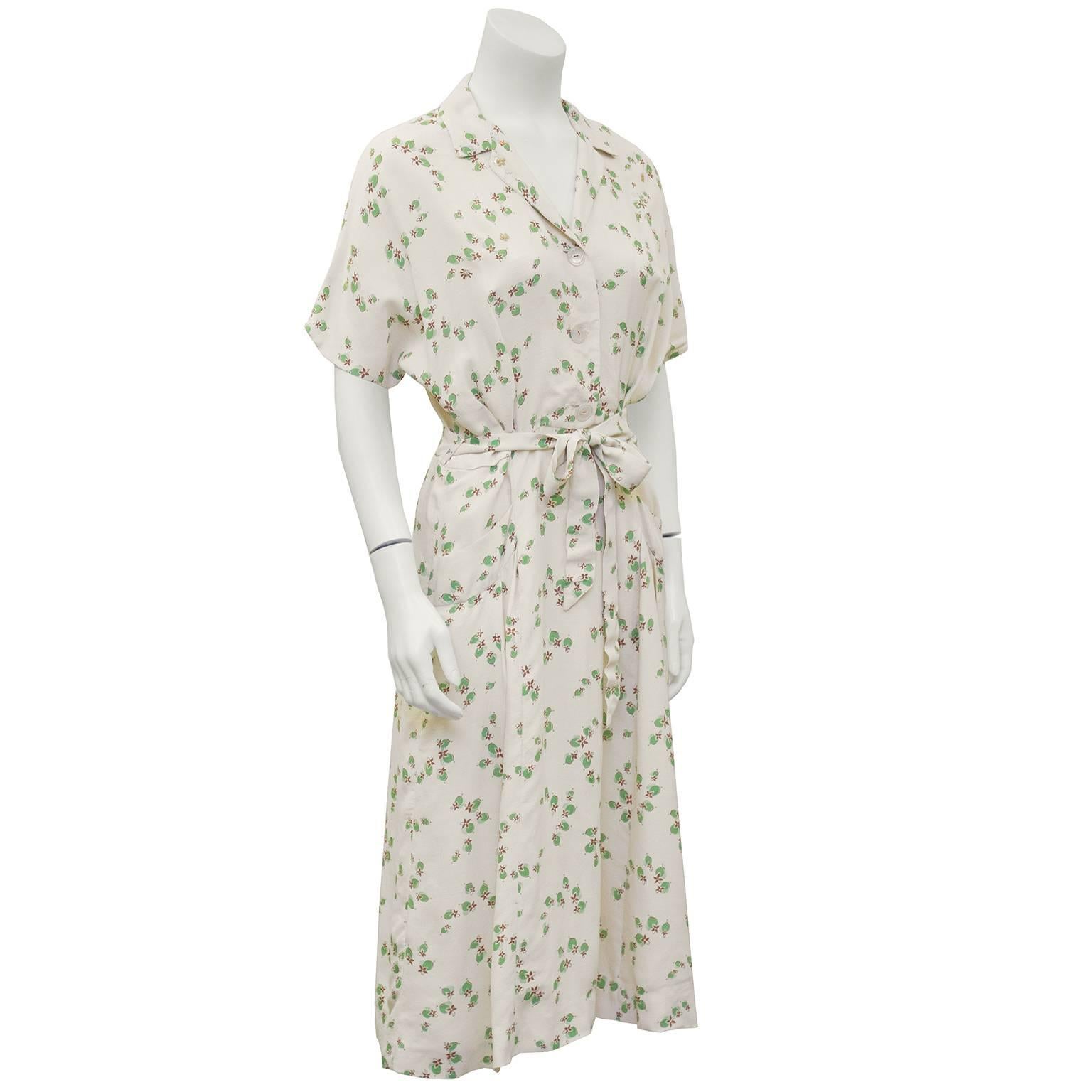 Beige rayon shirtwaist dress from the 1940's. The dress has an all over delicate print of green flowers with sequin and bead embellishments interspersed throughout. Buttons down the front and tie belt at the waist. Slight dolman style sleeve. In