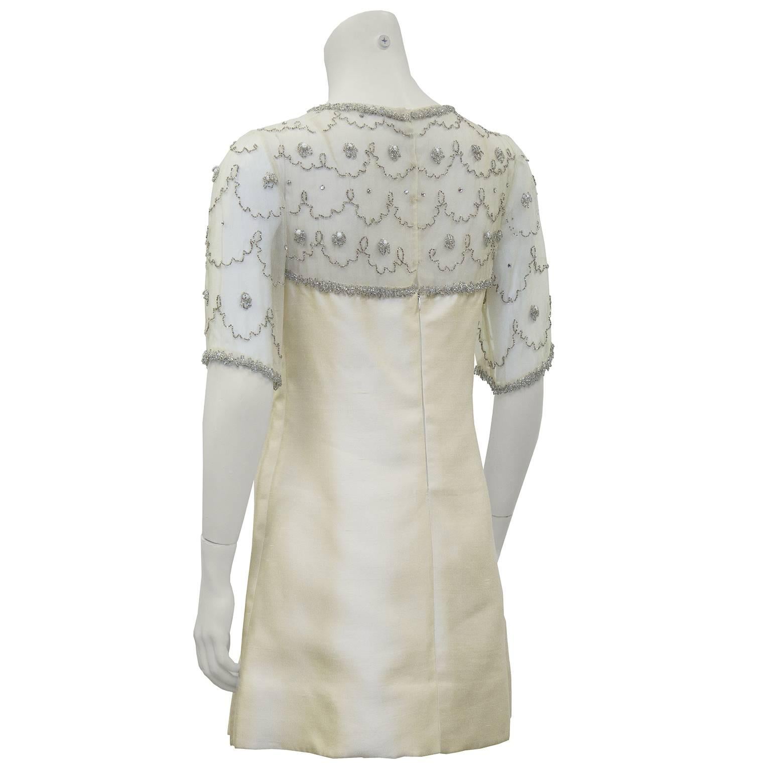 Adorable 1960's cream mini dress with beaded top panel. The round neckline and short sleeves are sheer and beaded all over with small silver beads in a scallop and flower pattern. Silk shantung bodice with seams down the front. In excellent