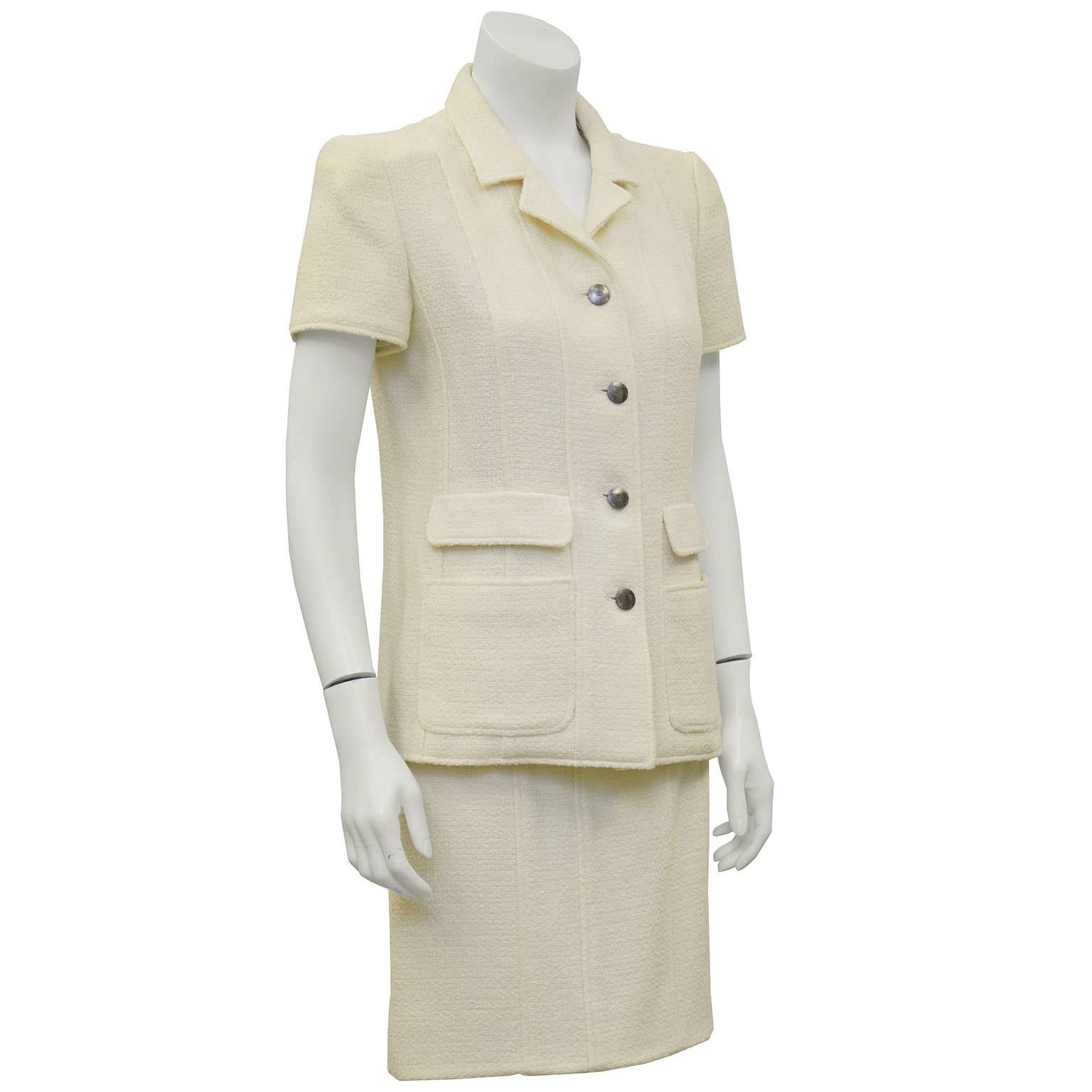 Chanel cream boucle wool and cotton blend short sleeve suit from the 1998 Spring collection. Short sleeve jacket with a notched lapel, silver Chanel buttons down the front and patch and flap pockets. Banded waist skirt with zipper up the back and