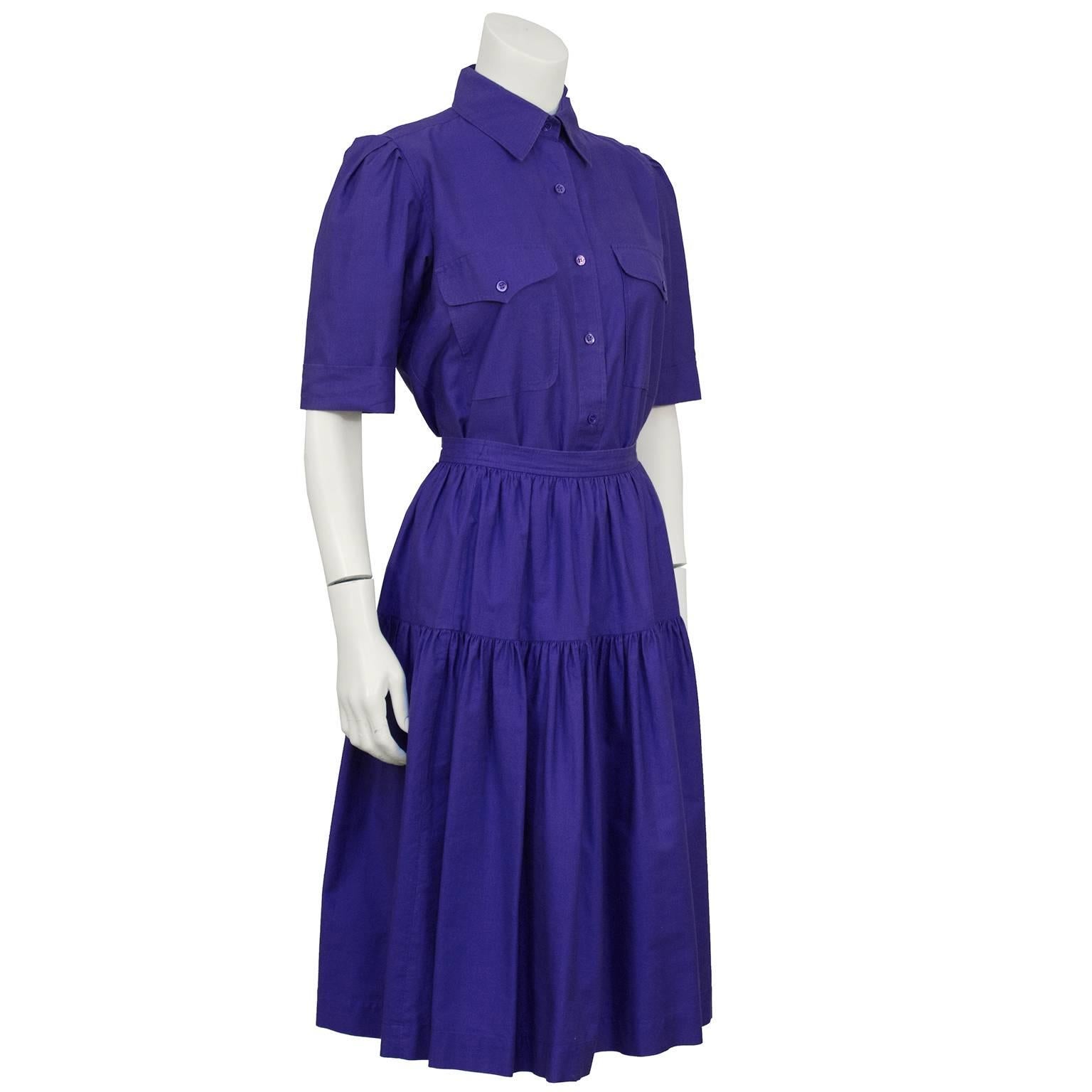 Purple cotton YSL skirt and button down ensemble from the 1970's. Collared shirt with small purple buttons down the front, top flap pockets on the bust and short sleeves. Yoke on the back, sleeves can be cuffed. Skirt has a banded waist, one tier