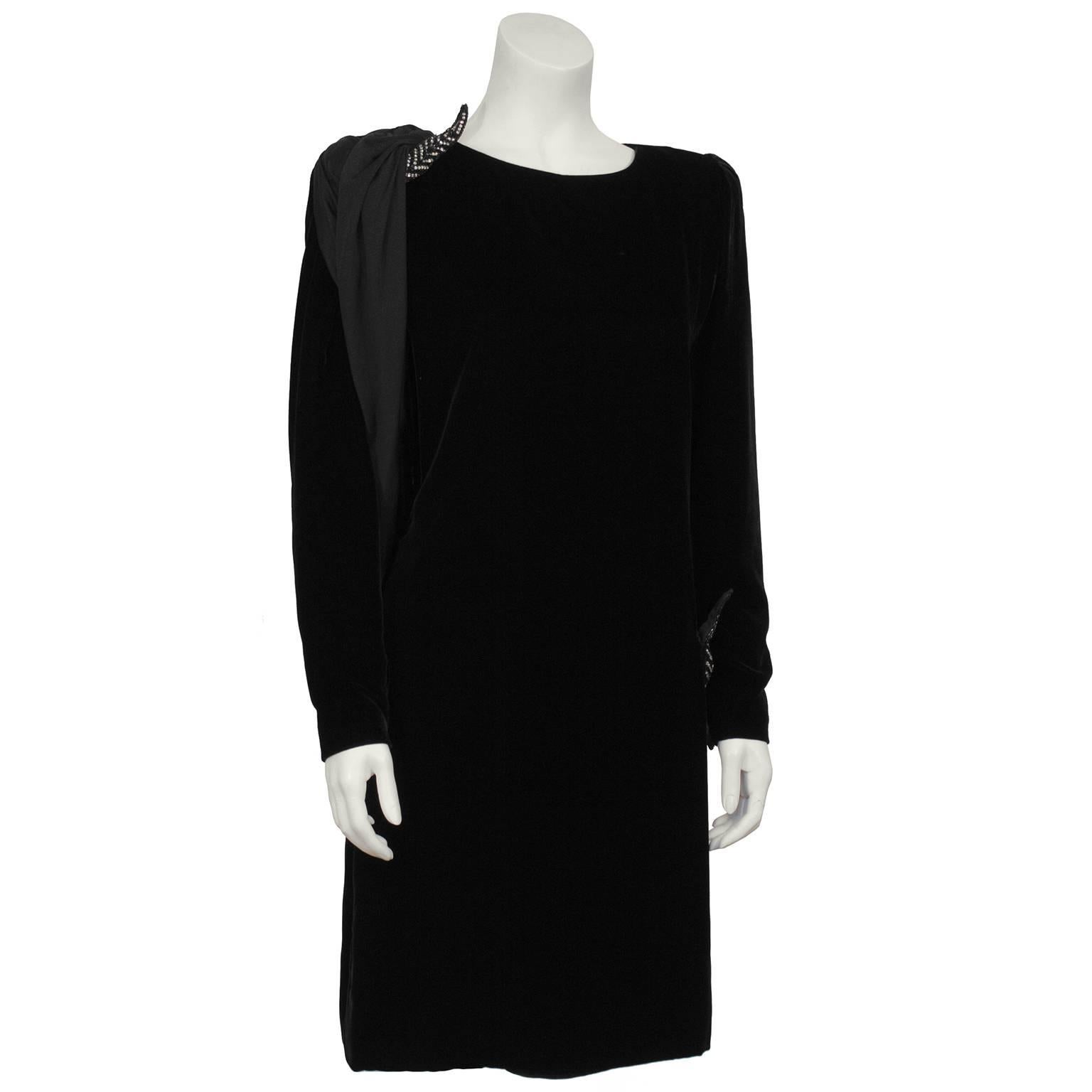 Long sleeve black velvet Valentino cocktail dress from the 1980's with a jersey sash detail. The dress has a boat style neckline, slight puffed shoulders and tapered sleeves with zippers at the wrists. The black jersey sash starts at the front of