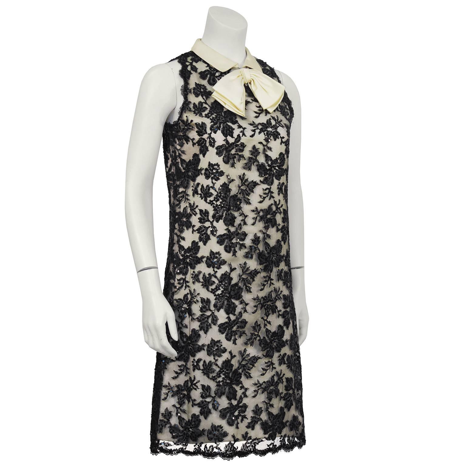 Beautiful 1960's cream satin sleeveless cocktail dress with a black lace over lay embellished with sequins. The dress has an off white satin collar that is finished with a static bow at the front of the neck. Zips up the back, unhooks at shoulder