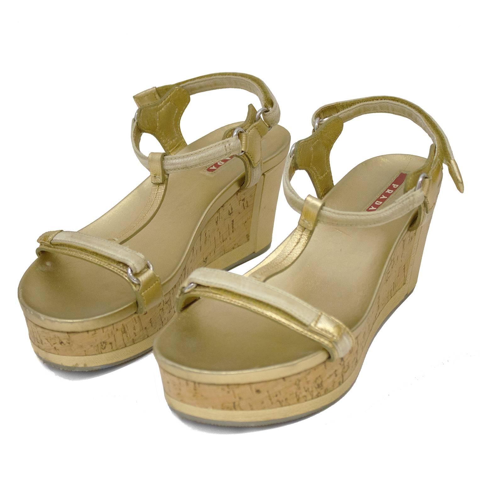 T strap gold leather platform sandals by Prada Sport from the 2000's. The cork sole is accented with a gold leather panel along the heel and the ankle straps fasten with velcro. Cream velvet details along the straps, silver hardware and grey