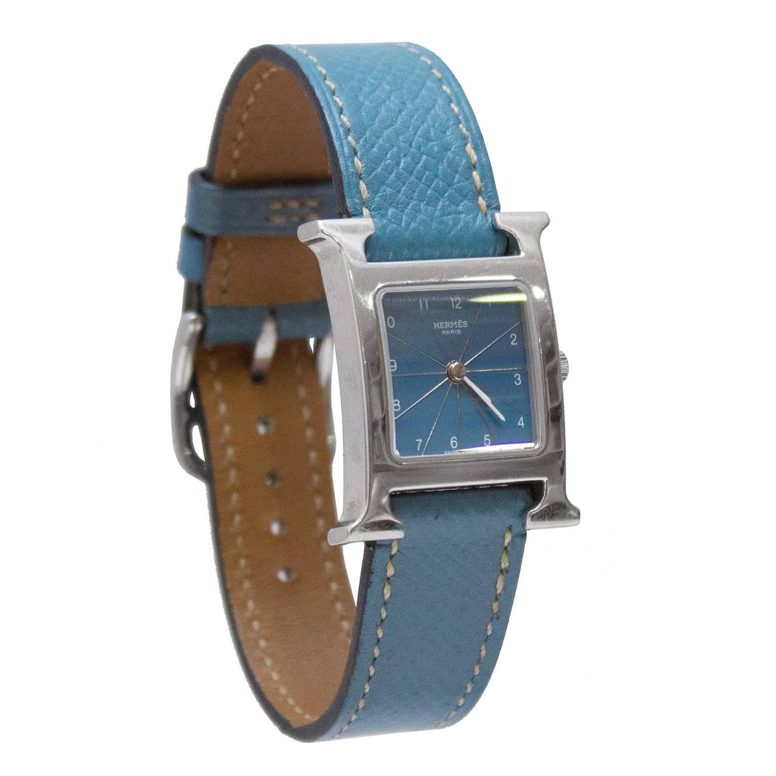 Beautiful Hermes Heure H watch from 2001. Stainless steel H shaped dial with a quartz crystal over a blue face, Arabic numerals and stick hands. The matching blue leather strap fastens with a tang buckle closure. Blind stamped with an E in a square