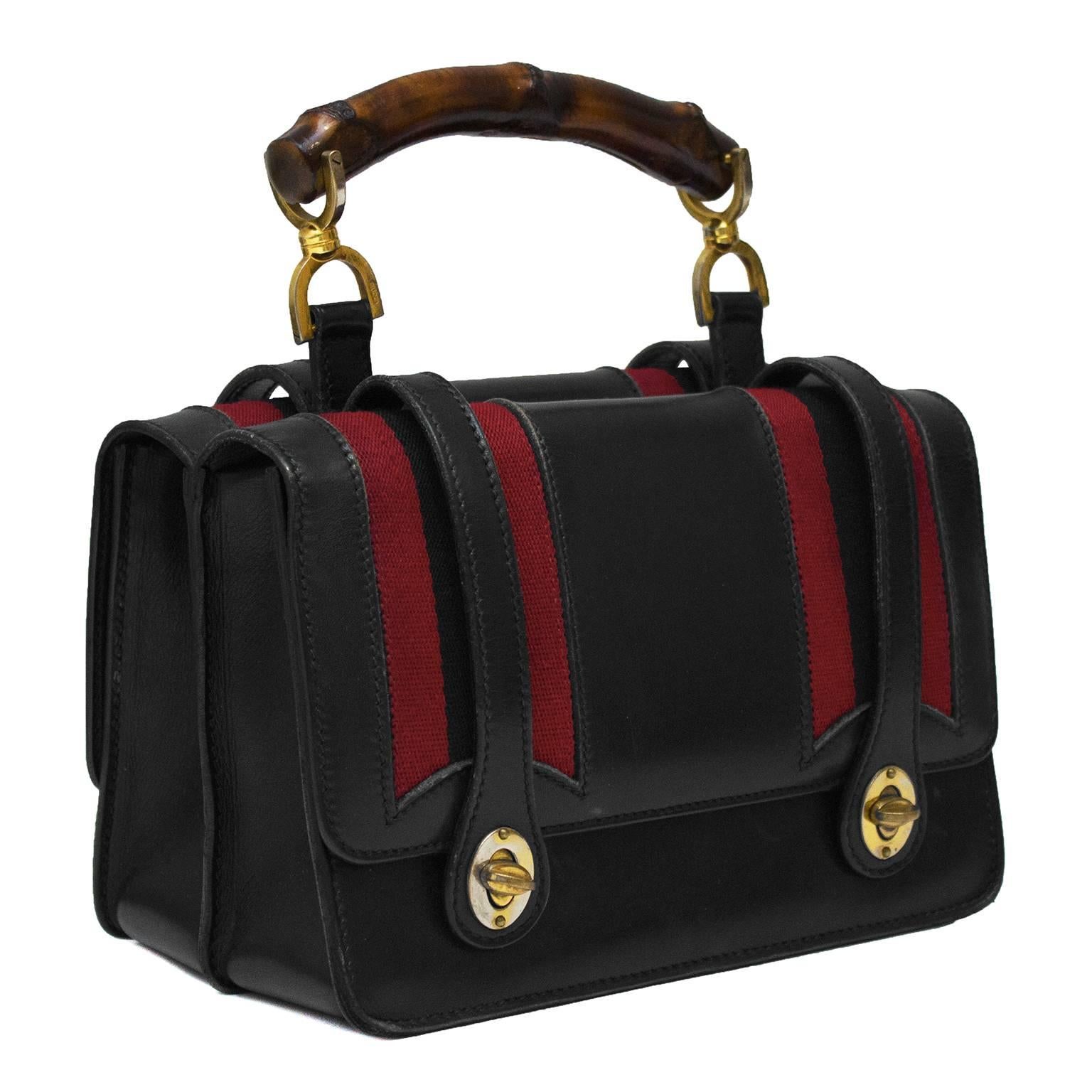 Gucci double compartment black leather handbag from the 1960's. The bag has two identical top flap pocket compartments on either side with red fabric stripes down the side. Closes with two turnlocks on either end and finished with a wooden bamboo