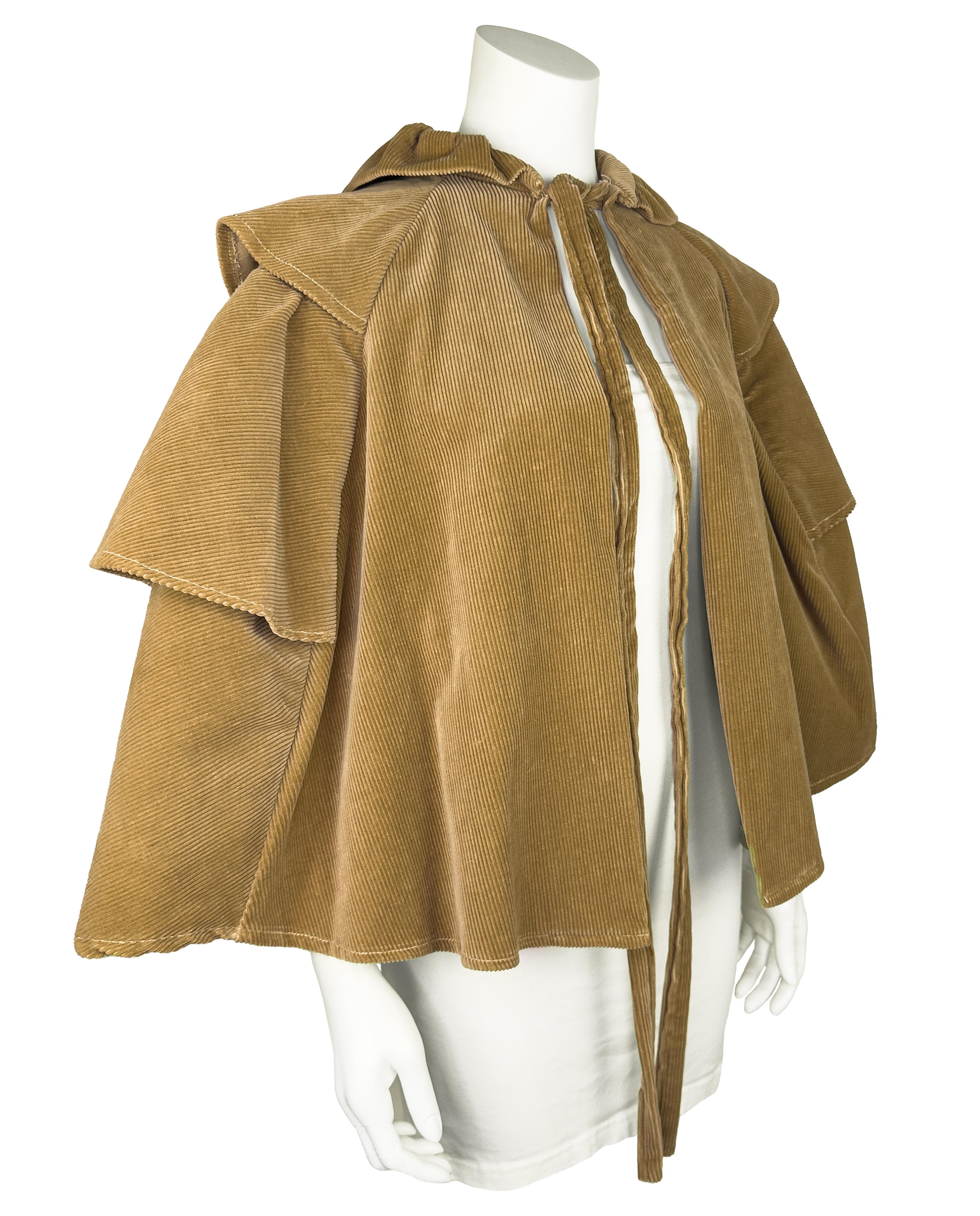 Avvolgiti in un fascino da libro di fiabe con questa mantella di Laura Ashley degli anni '60. Realizzato in velluto a coste color marrone, questo capo presenta una silhouette voluminosa con tre grandi volant, una schiena sapientemente drappeggiata,
