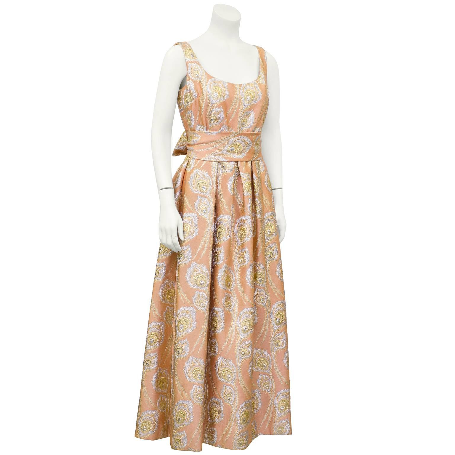 Ceil Chapman gown dating from the late 1960s. Beautiful muted peach and metallic brocade featuring peacock feathers all over. Scoop neck, empire waist and full skirt. Optional matching sash to tie at waist. Very good vintage condition, slight wear