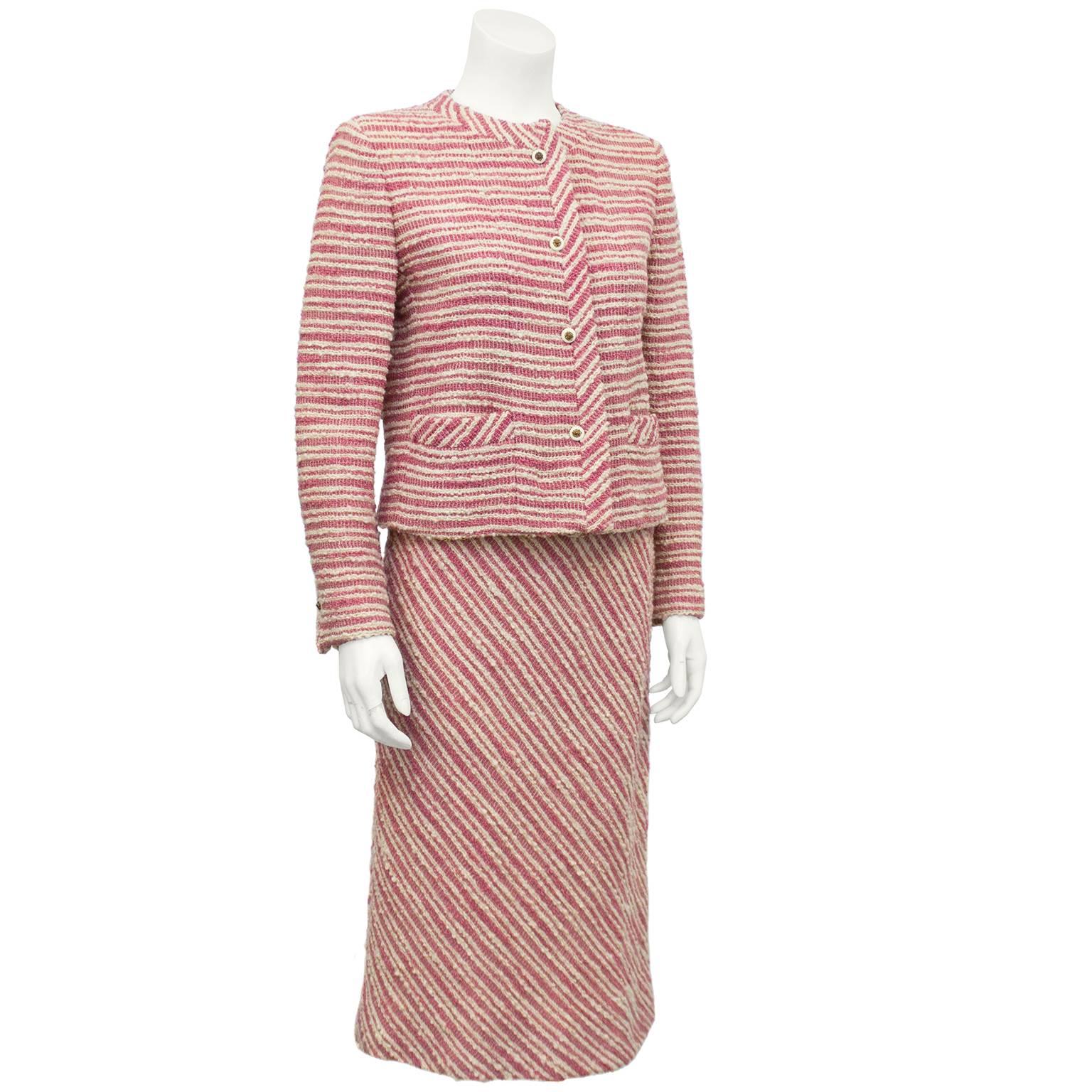 1970s Chanel Creations label pink and cream boucle striped skirt suit. The jacket is in the classic Chanel style with a rounded neckline and pockets accented with the matching pink and cream striped fabric on a diagonal. Cream buttons with lions