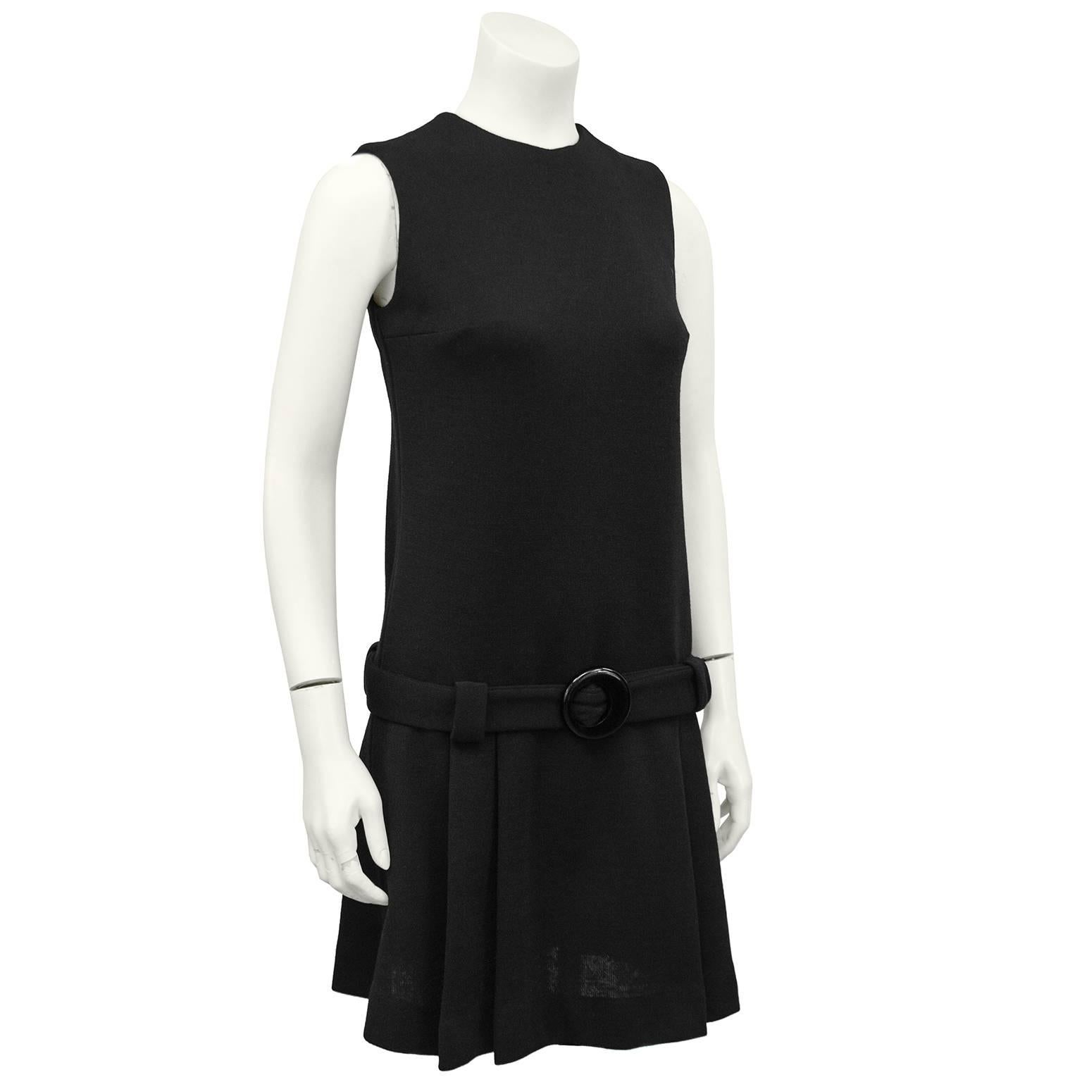 A classic LBD from the 1960s by American designer, Jonathan Logan. The sleeveless dress has a drop waist and a box pleated skirt. A matching black fabric belt at the dropped waist is accented with a black circular buckle. Zips up the back. In