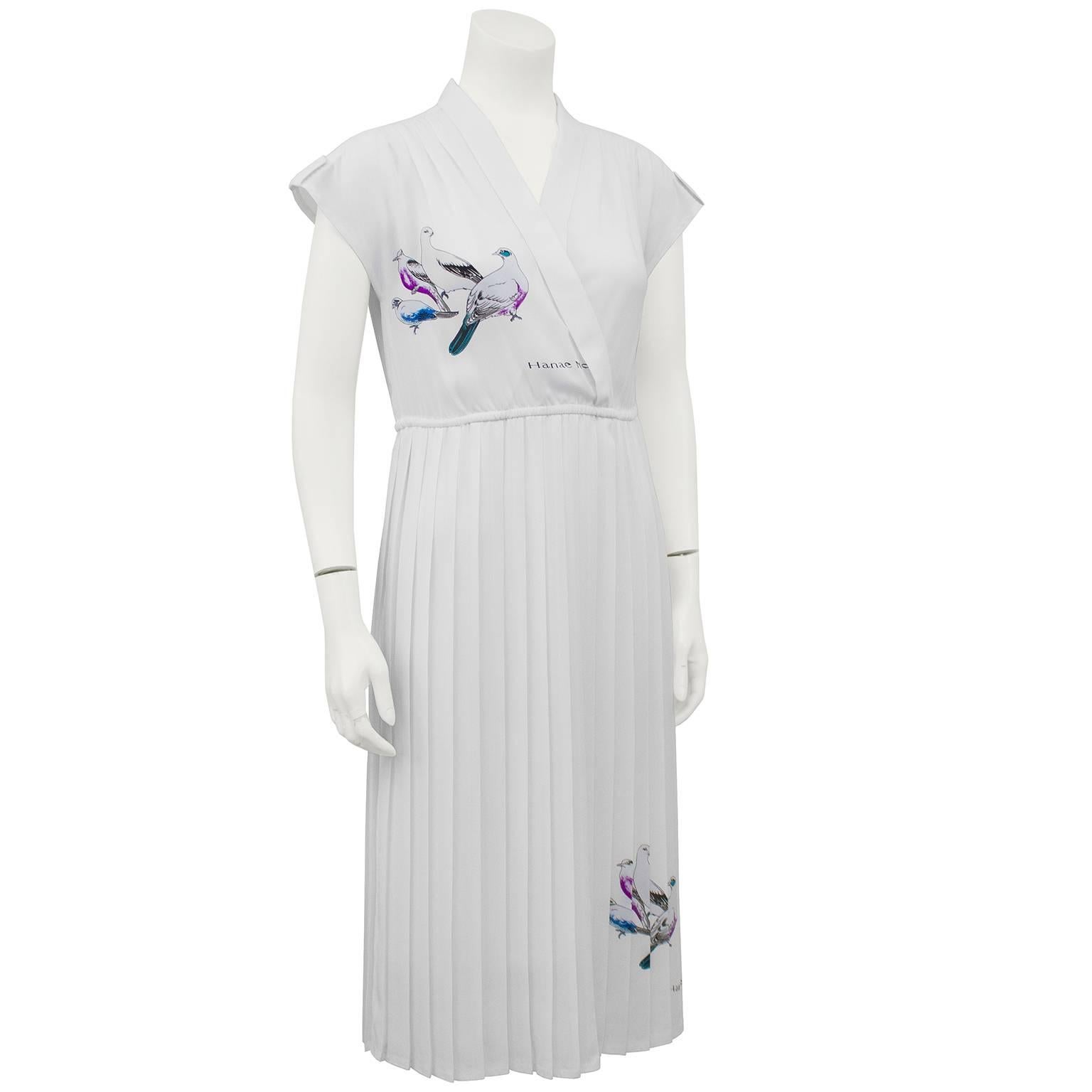 1970s Hanae Mori white silk dress with cross over neckline, gathered elastic waist and a pleated skirt. The cap sleeves have tiny epaulets with Hanae Mori logo buttons. The dress features two beautiful silk screened images of birds; one on the bust