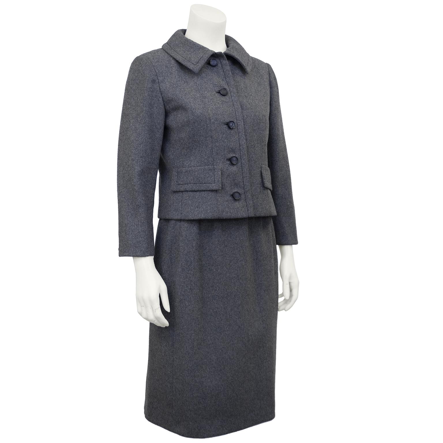 A classic style Christian Dior New York grey wool suit from the Los Angeles luxury department store Bullock's Wilshire. The collar and faux pocket top flaps have a black contrast stitched border detail and the fitted cropped style jacket does up the