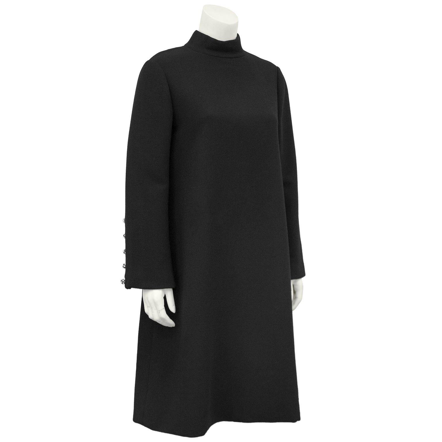 Beene at his very best, this 1960s black wool cocktail dress is the epitome of understated chic. The bell sleeves are accented with round rhinestone buttons and the A line swing style dress is cut perfectly. Zipper up the back with two hooks at the