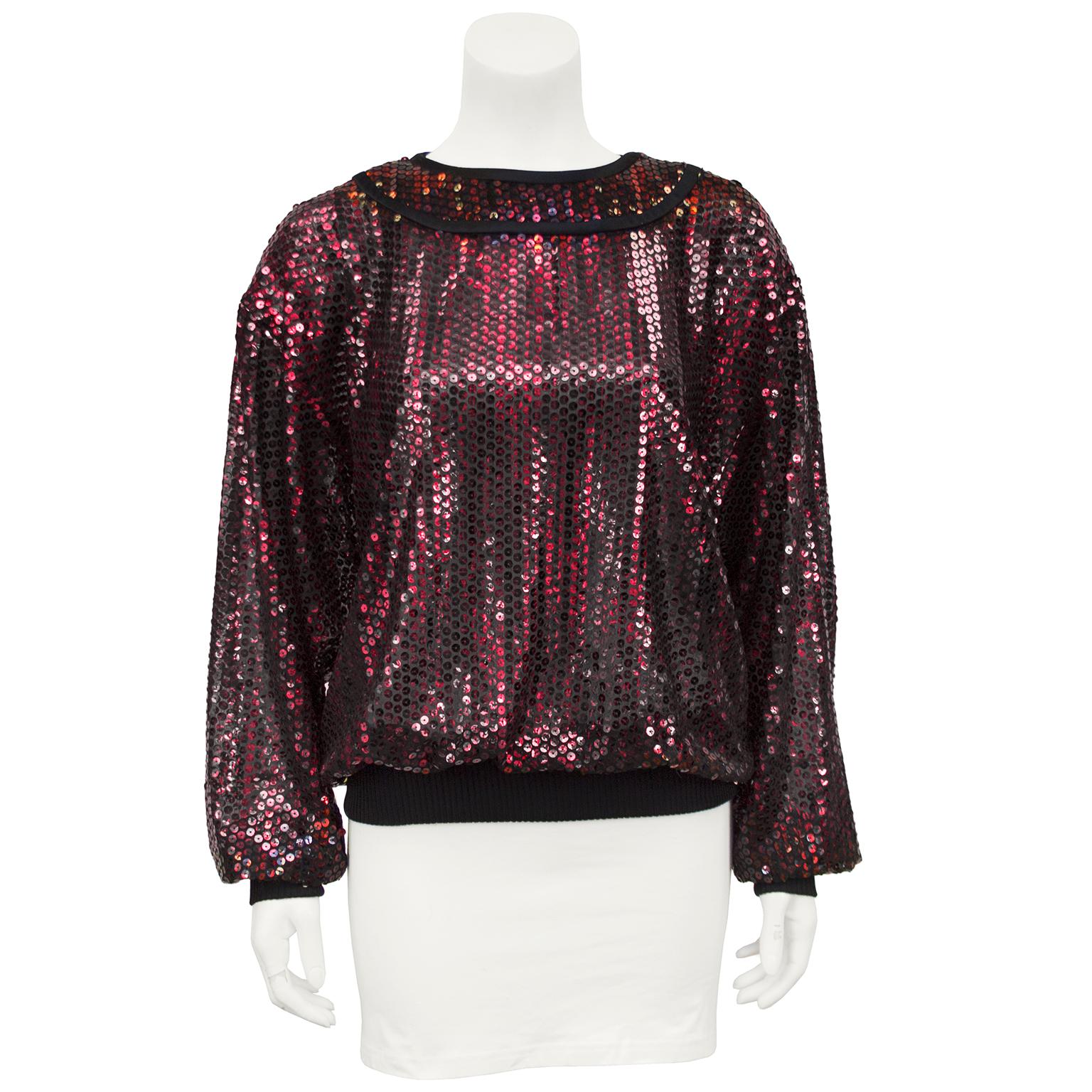 Emanuel Ungaro 1970s red sequin top with black ribbing at the cuffs and hem. The fit is blouson, almost sweatshirt style, with a black stain trimmed yoke at the neckline and 3 black faceted buttons on the top of the let shoulder. The res iridescent