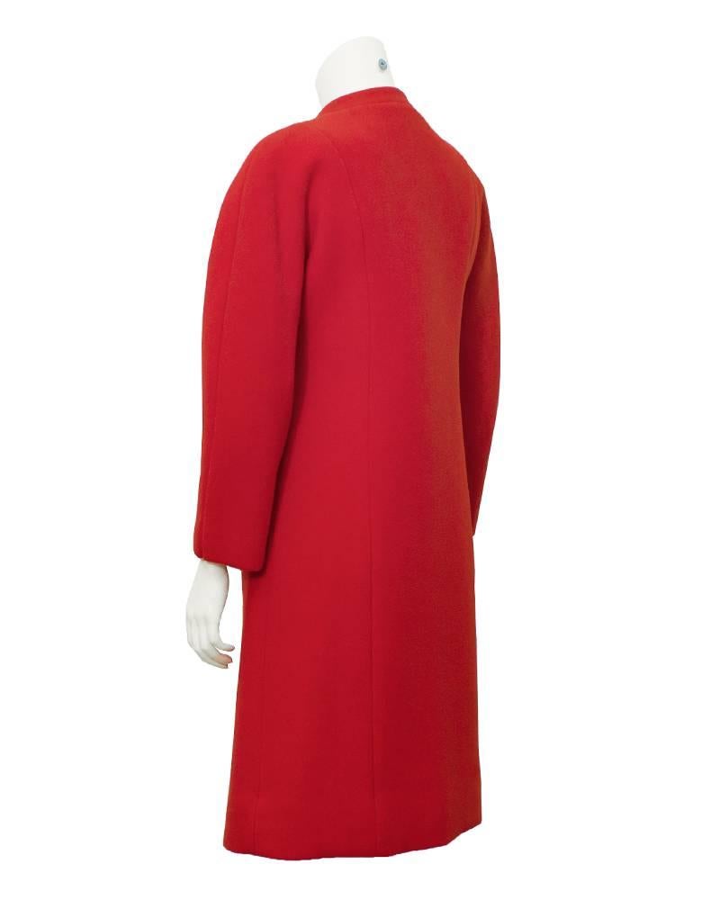 A vibrant red 1960's Haute Couture Jacques Heim wool coat. The deep red coat is accented with jet black domed buttons down the front and a simple mandarin collar. Two bold seams run down the front with tiny placket trimmed slip-in pockets. Shoulders