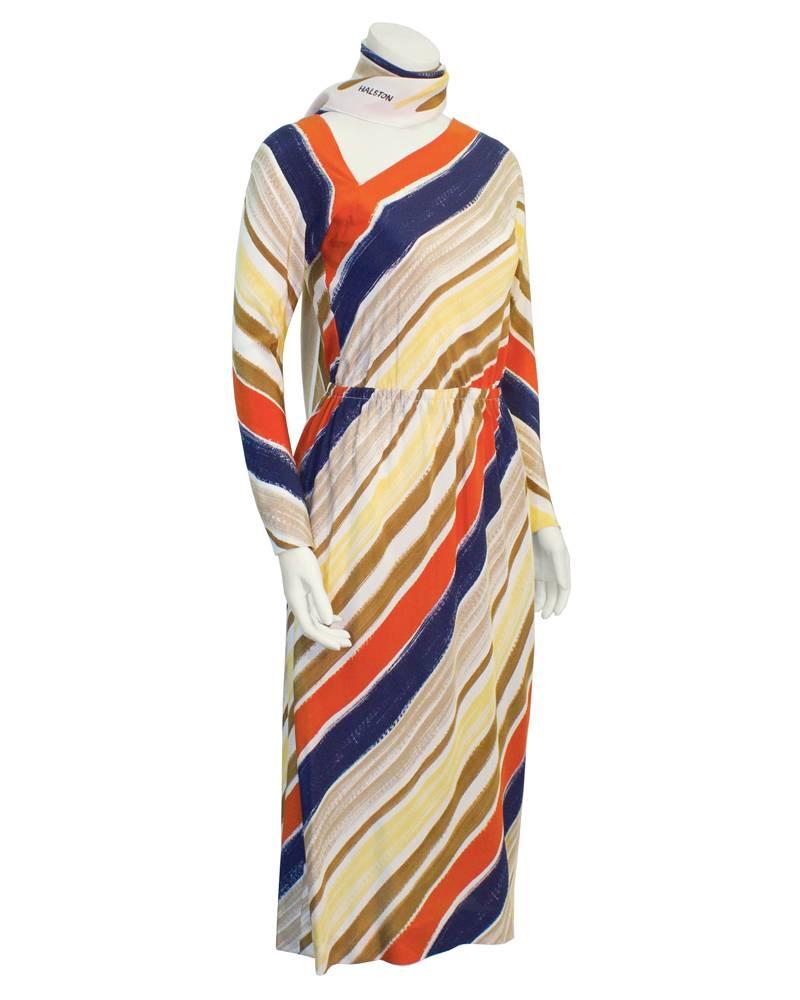 Asymmetrical cut Halston silk dress from 1977. Navy blue, orange, tan, brown, pale yellow and cream diagonal stripe print. Long sleeves, asymmetrical neckline and elastic waist. Matching stripped neck/waist tie with Halston signature logo. Excellent