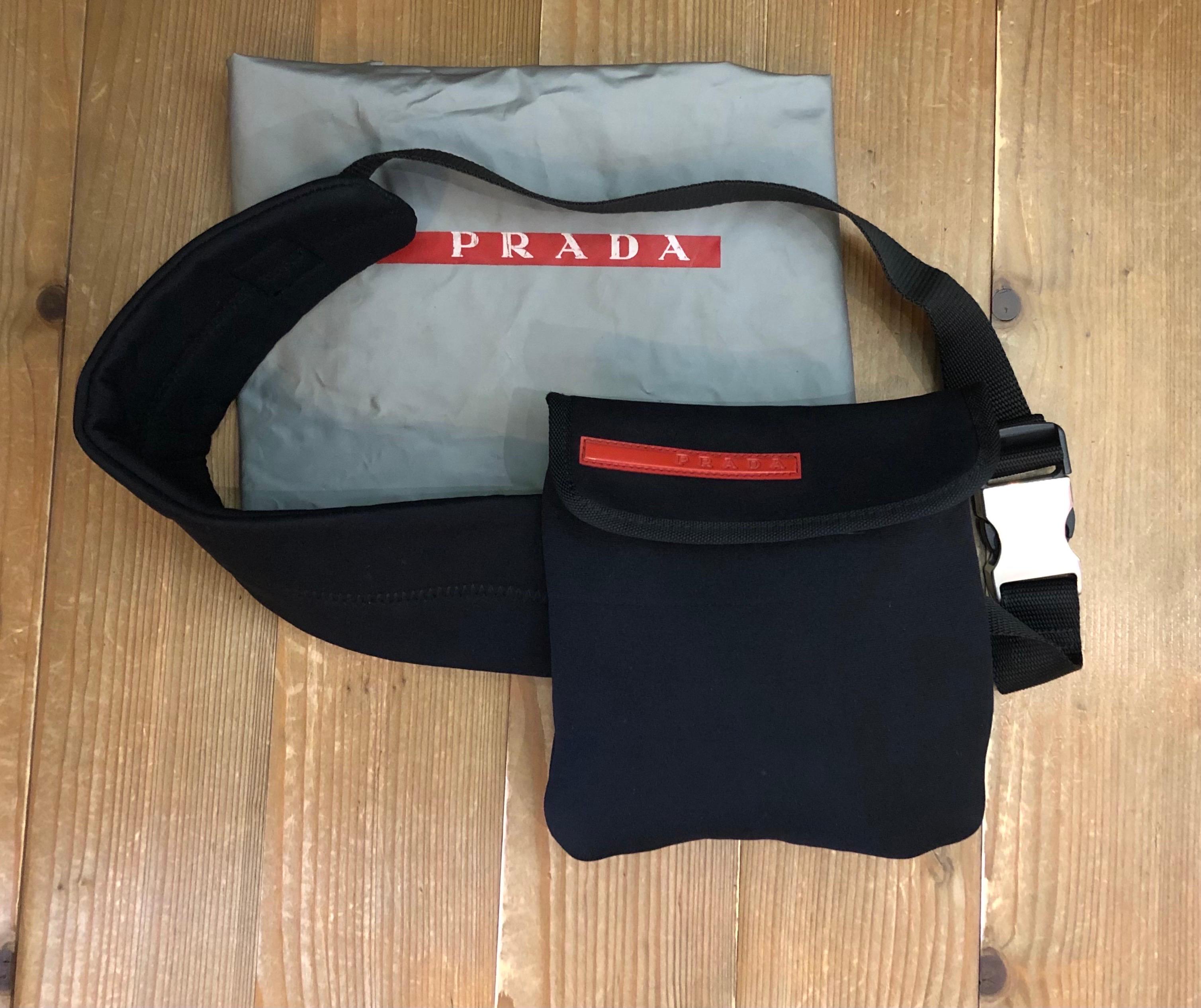 Ce sac vintage PRADA Steel-Line est fabriqué en microfibre légère de couleur noire et comporte une ceinture amovible en microfibre et polyester avec une boucle réglable en acier inoxydable. Le rabat avant à fermeture velcro s'ouvre sur un intérieur