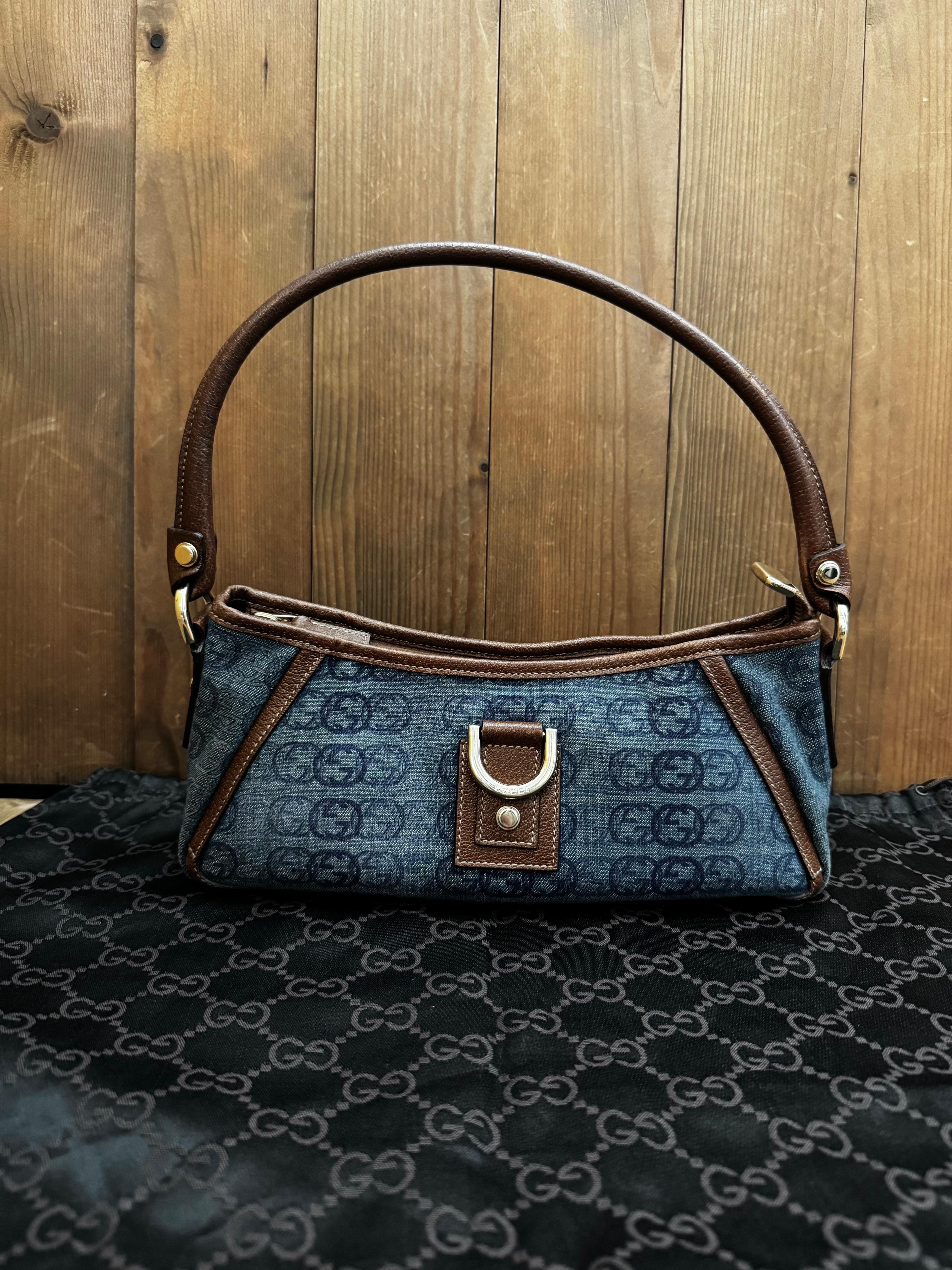 This vintage GUCCI D-ring Abby baguette bag is crafted of Gucci GG monogram stone-washed blue denim and brown leather featuring light gold-toned hardware. Top zipper closure opens to a brown fabric interior with a patch pocket. Made in Italy.