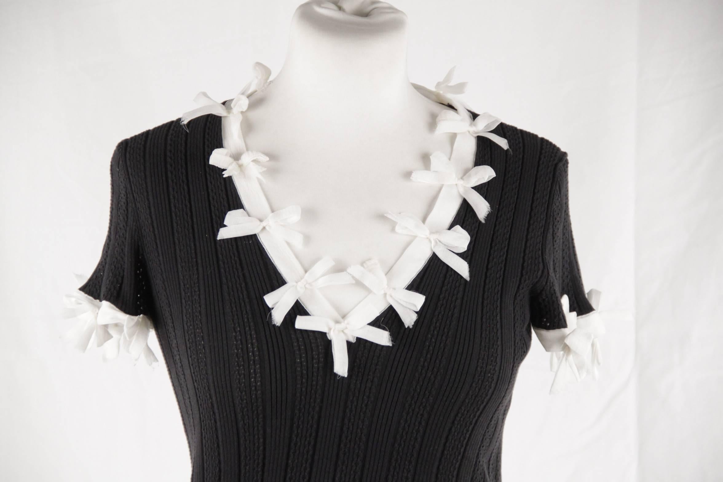 - Black Chanel knit top with short sleeves
- V-neck and rib knit trim
- Accented with white silk bows around collar and sleeves
- CHANEL embossed on a iridescent plaque on the lower left side
- Composition: 100% cotton / Insert: 100% silk
-