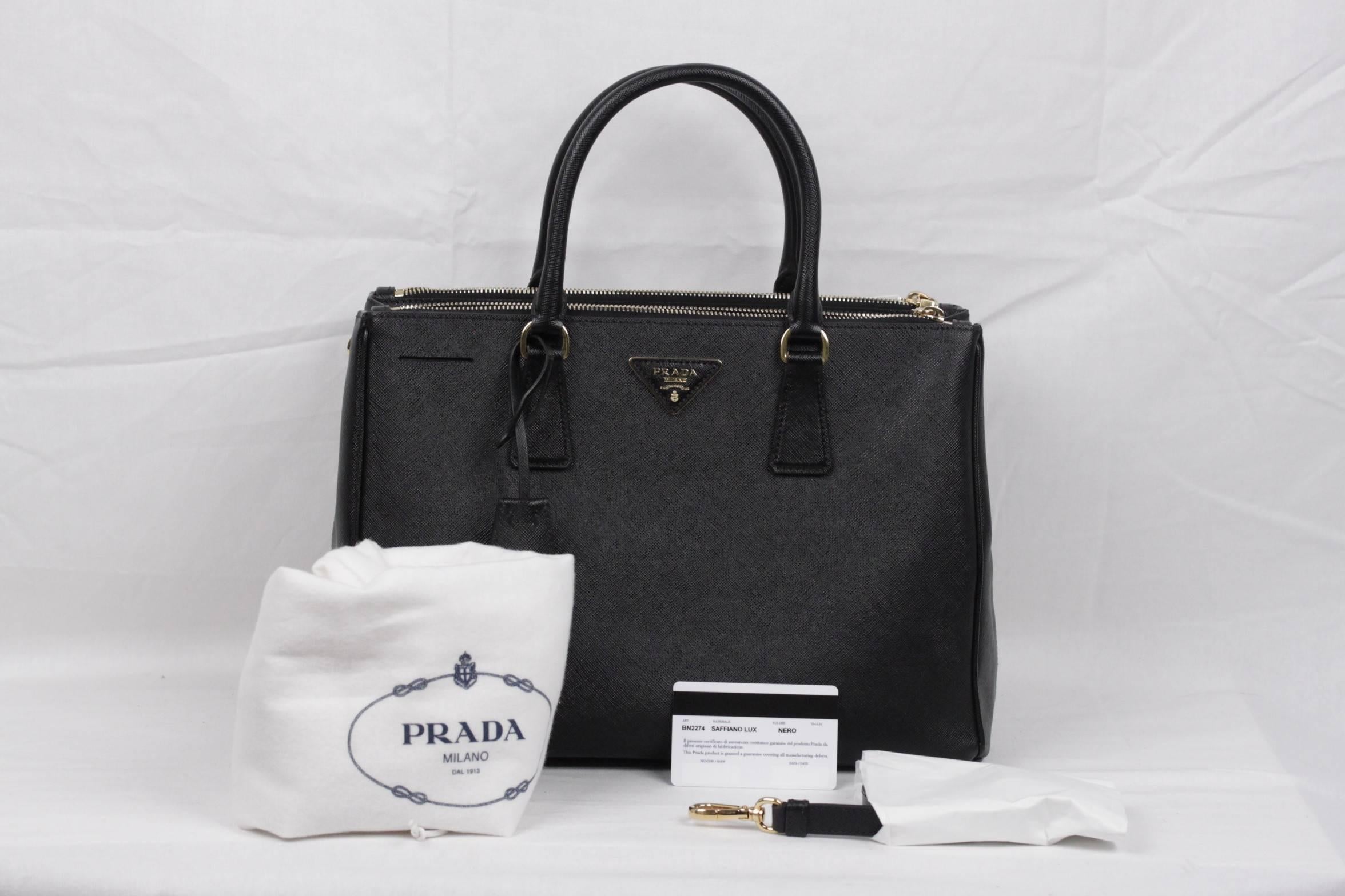  Stunning PRADA top handles bag/handbag mod. BN2274, designed in black Saffiano Lux leather and finished with gold metal logo lettering on the front, all in a structured tote silhouette. It features a removable keychain with leather clochette,