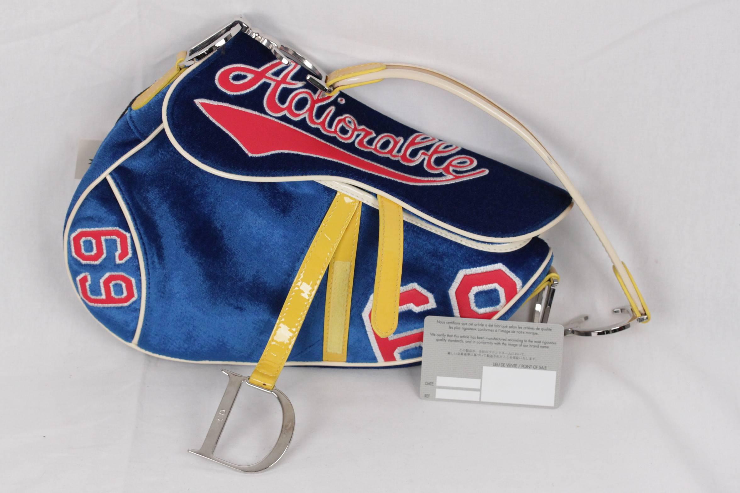 
- Limited Edition Blue velour velvet Christian Dior 'Adiorable' Saddle bag
- Yellow patent leather handle and trim
- Embroidered red leather 'Adiorable' and '69' numbers at front
- Back pocket
- Flap top with velcro closure
- Monogrammed navy