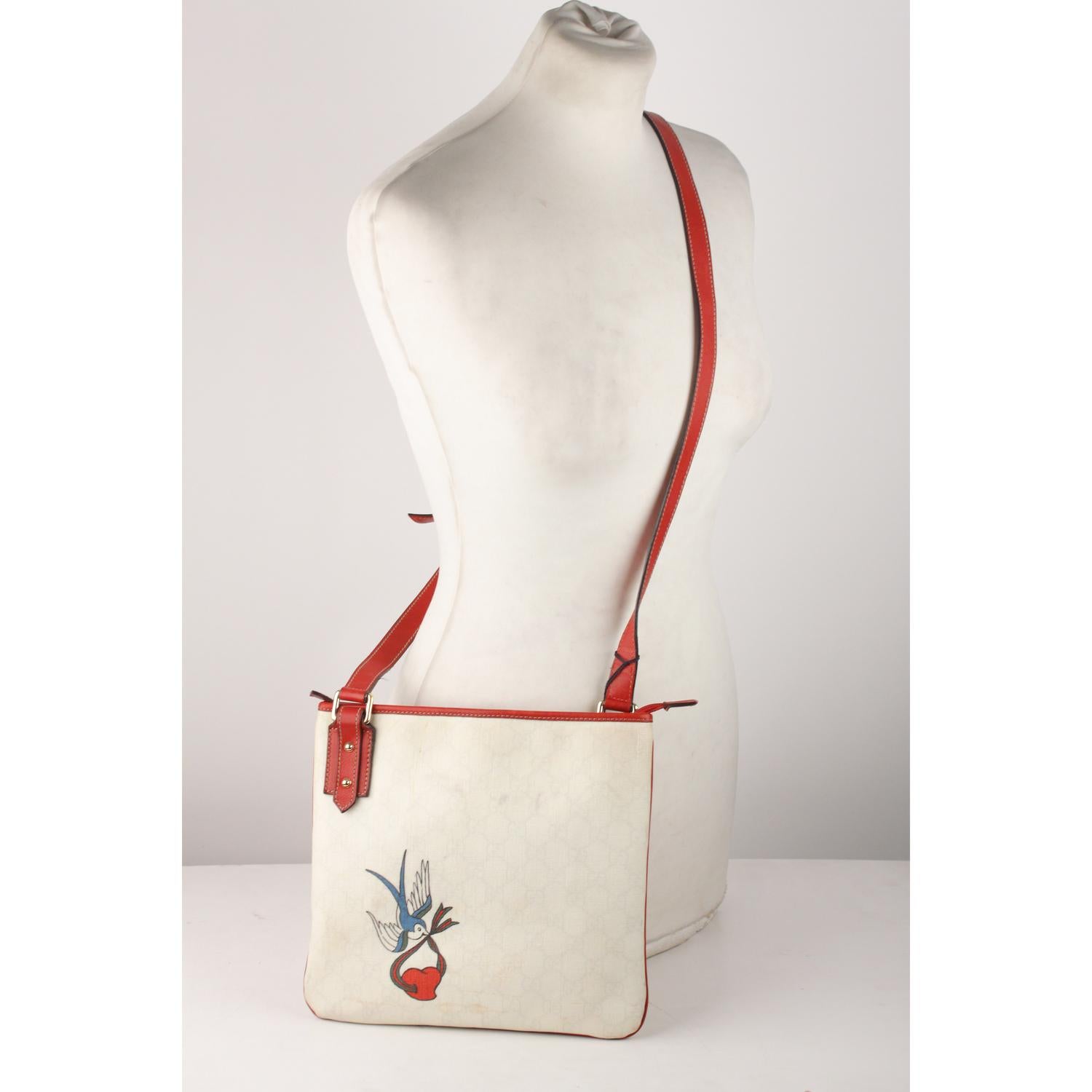 Gucci messenger bag made of white monogram canvas with beautiful birf tattoo detail on the front. Red trim and adjustable shoulder strap. Upper zipper closure. Red monogram fabric lining with1 side zip pocket inside. 'GUCCI - Made in Italy' tag