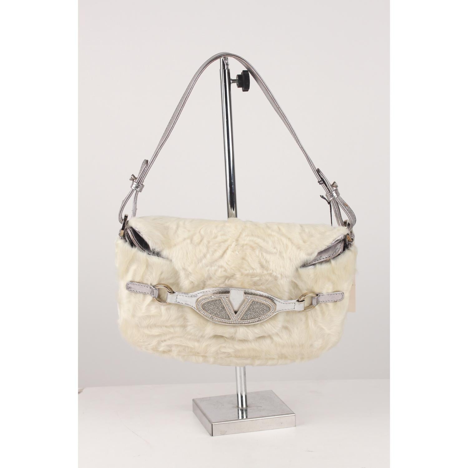 Sophisticated Valentino Garavani  shoulder bag crafted in white fur and silver leather.  The front flap closure is embellished with crystal studded Valentino logo. It features a double flap design and an adjustable shoulder strap. Satin lining with