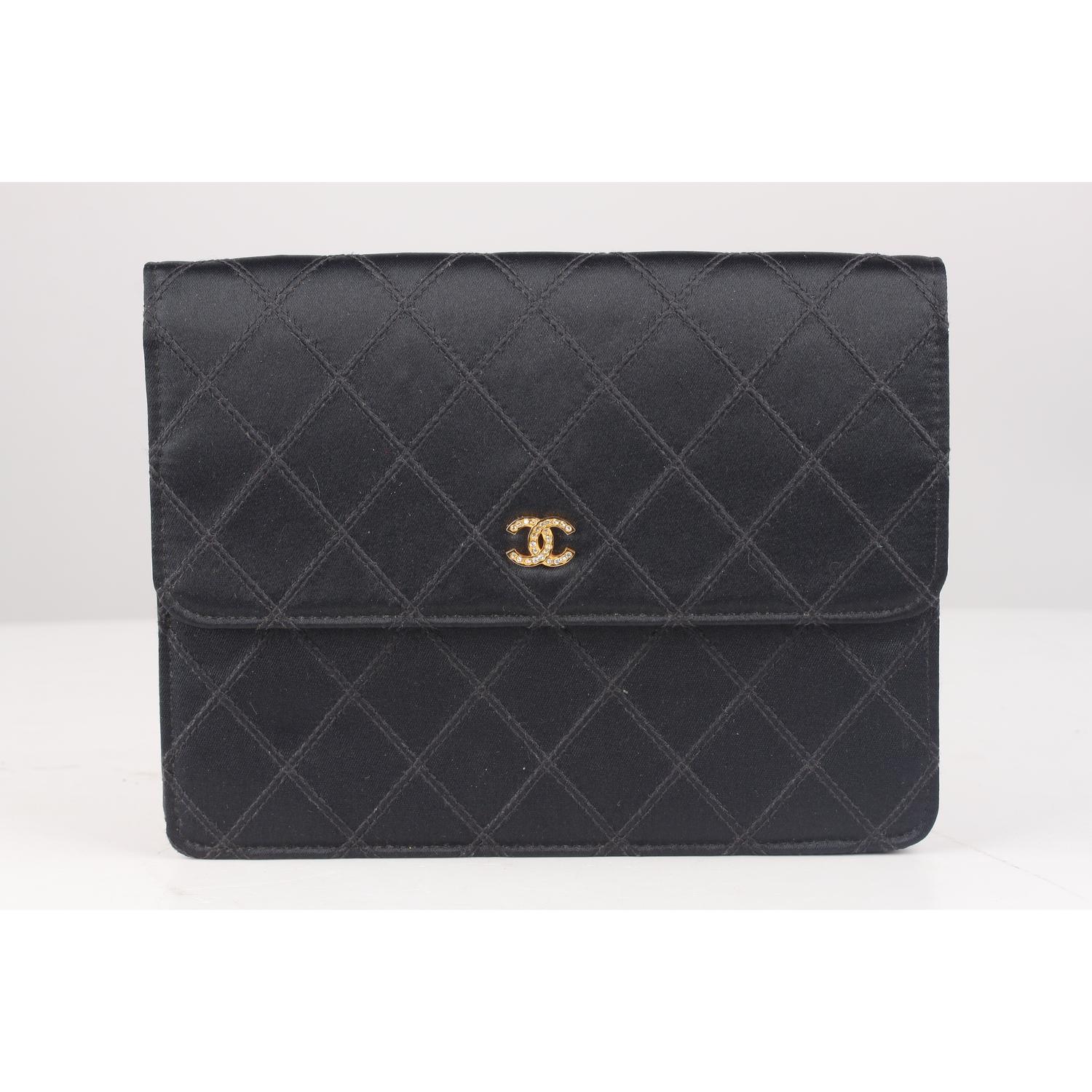 Vintage Chanel black quilted satin small clutch from the late 80s - early 90s. Flap with button closure. Gold metal CC - CHANEL logo on the front embellished with rhinestones. 1 open pocket on the back. Leather and gros-grain lining interior. 1 side