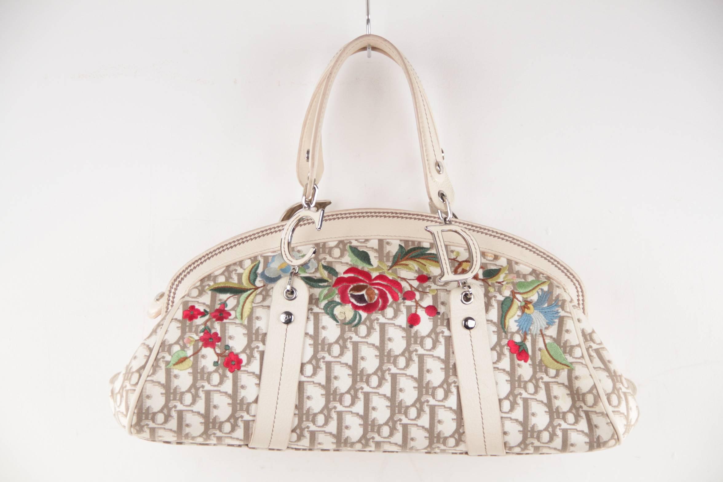  - Beige and white 'Diorissimo' canvas Christian Dior handle bag
- Multicolor floral embroidery at front face
- Silver-tone hardware
- Gleaming silver C and D hardware
- Upper zipper closure
- 5 protective bottom feet
- Dual flat handles
-