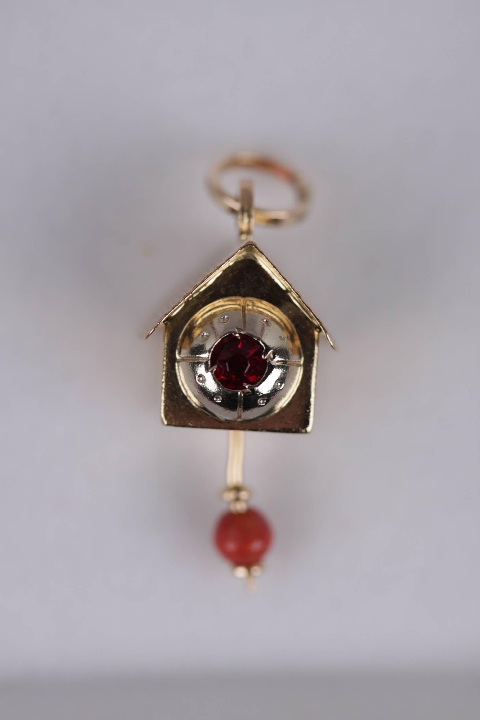 - Vintage 18k Yellow gold pendant in the shape of a cuckoo clock

- 'Engraved '750' hallmark on pendant 1AR

- Faceted ruby stone on the front

- Moving bead pendulum

- Comes with a red velvet case

- Total lenght: 2,5 cm - 1