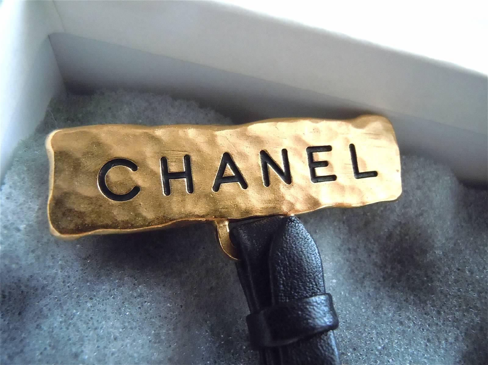 This extremely rare and fun design brooch was from 94 Spring.
Rich hammered thick pure gold like finish pin bar hanging a lambskin leather wrapped brooch drop.  
There are some fun info on the brooch, that reads, CHANEL PARIS,  phone number and