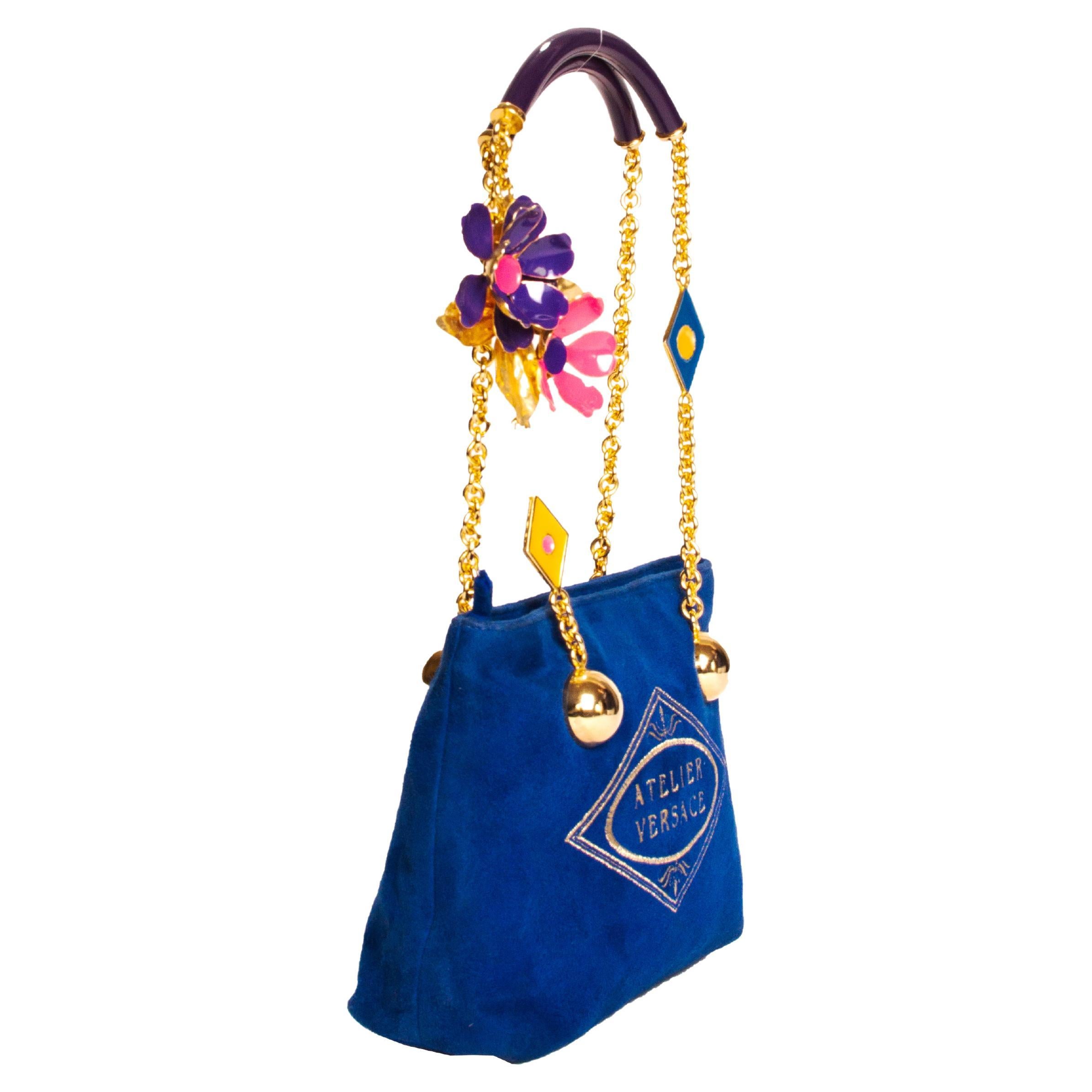 From the Spring/Summer 1991 collection, this bag designed by Gianni Versace features the 'Atelier Versace' embellished with gold thread prominently on both sides. The body of the bag is constructed with a bright royal blue faux suede. The straps of
